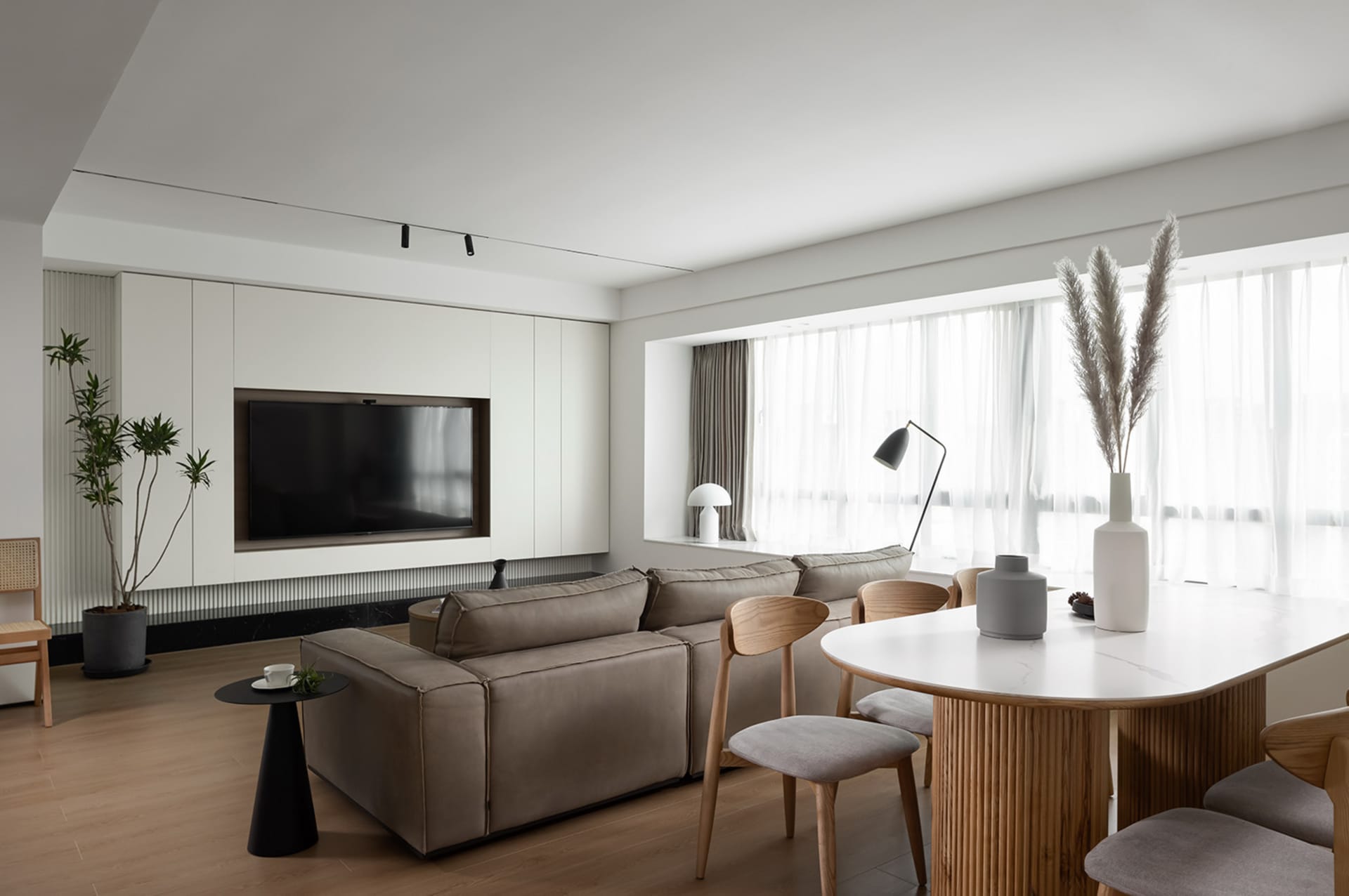 A modern living room featuring mixed materials with a focus on a large sectional sofa, white cabinets, and a white dining tab