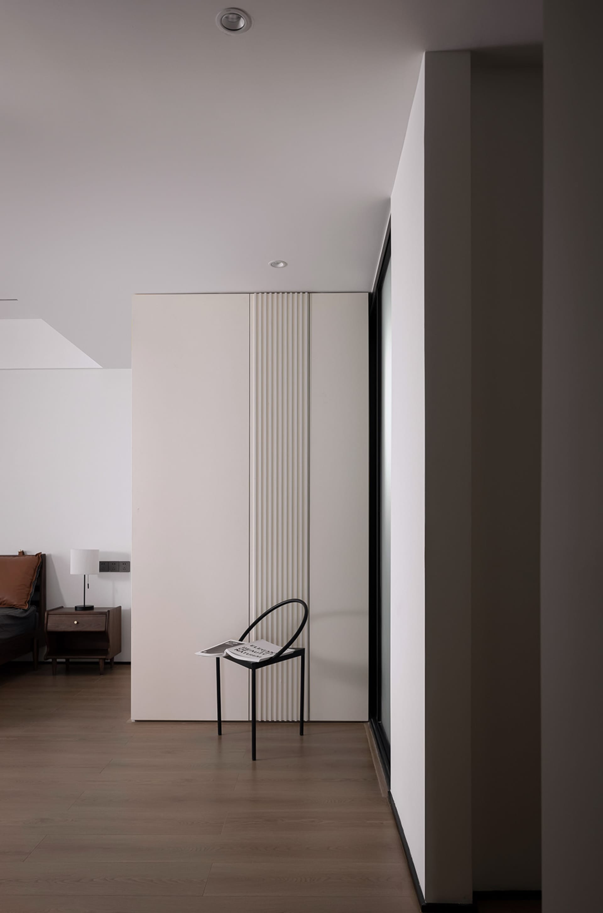 A modern minimalist bedroom featuring a white metal chair and minimal decor.