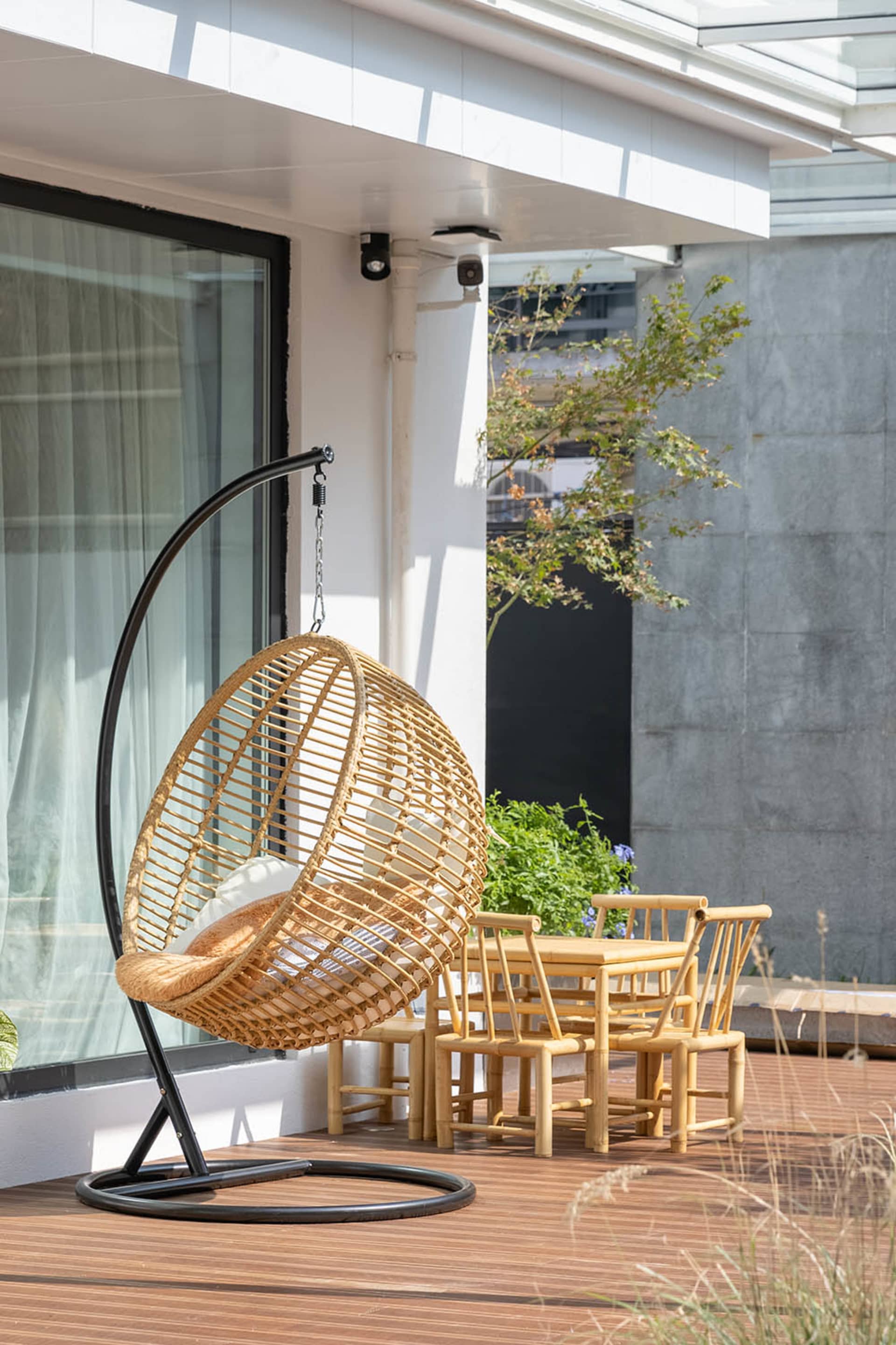 Bamboo-woven hanging chair and wooden dining set on a wooden patio