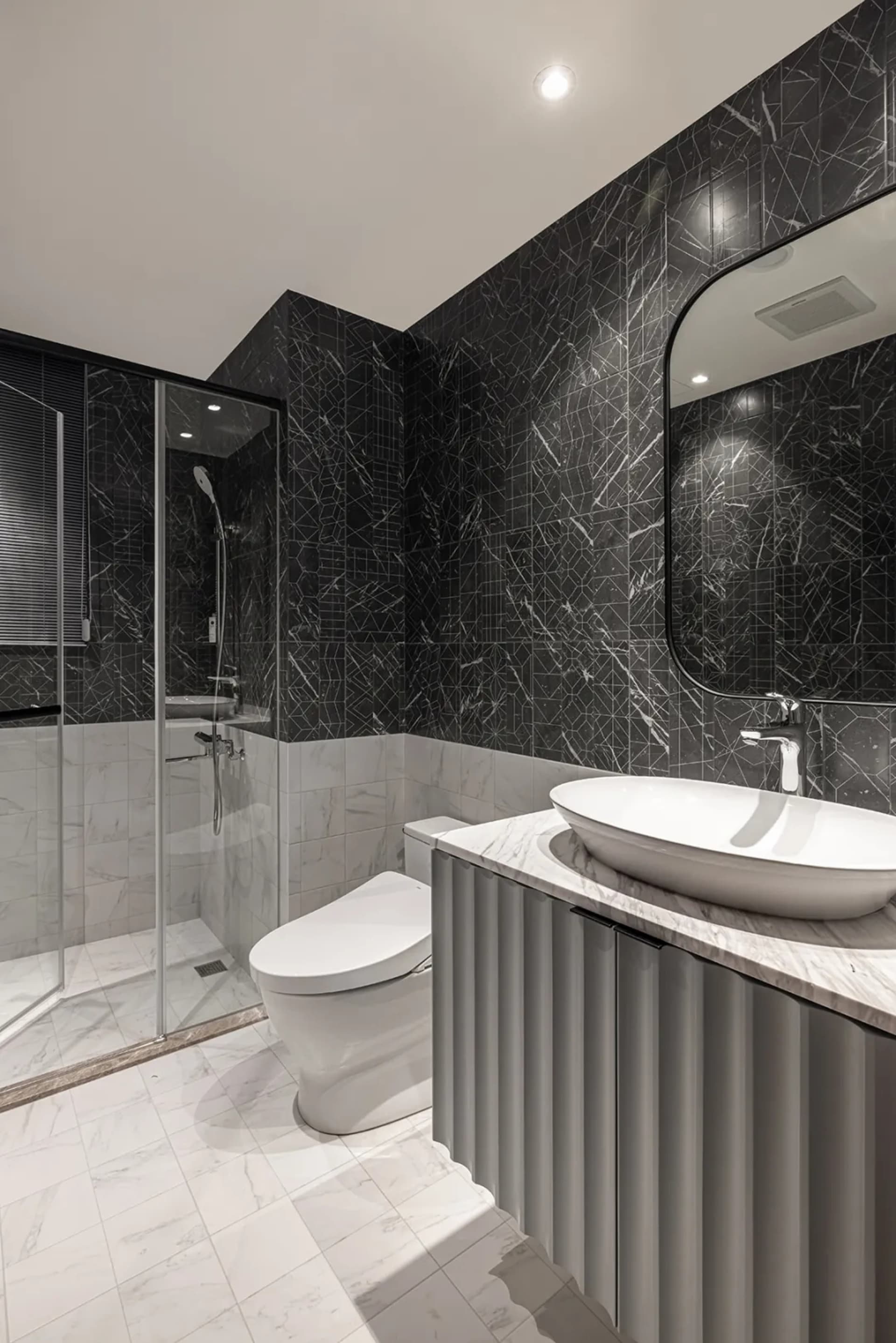 A modern residential bathroom with marble tiles, metal accents, and a white toilet.