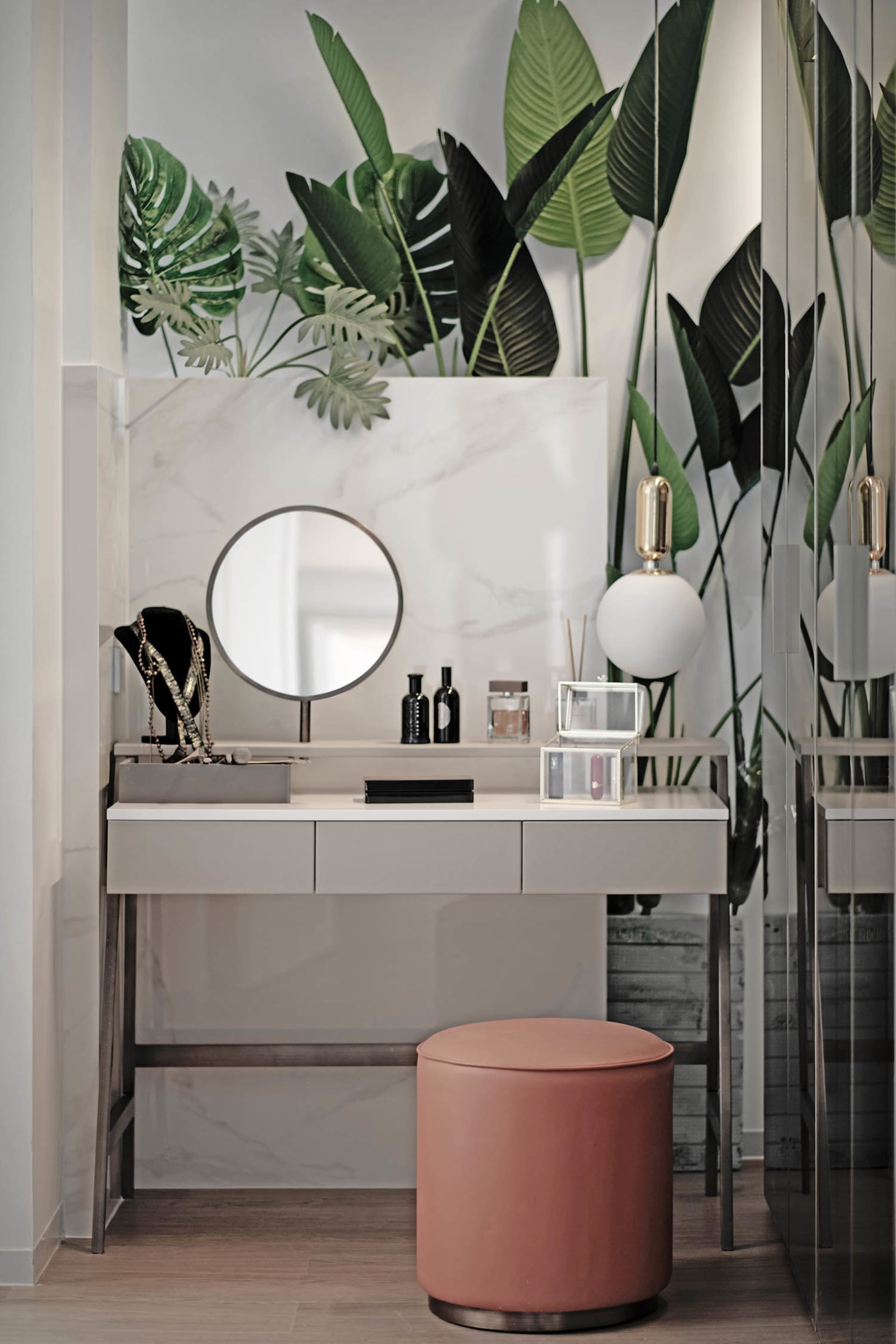 A modern vanity table with a round mirror, marble top, and pink stool.