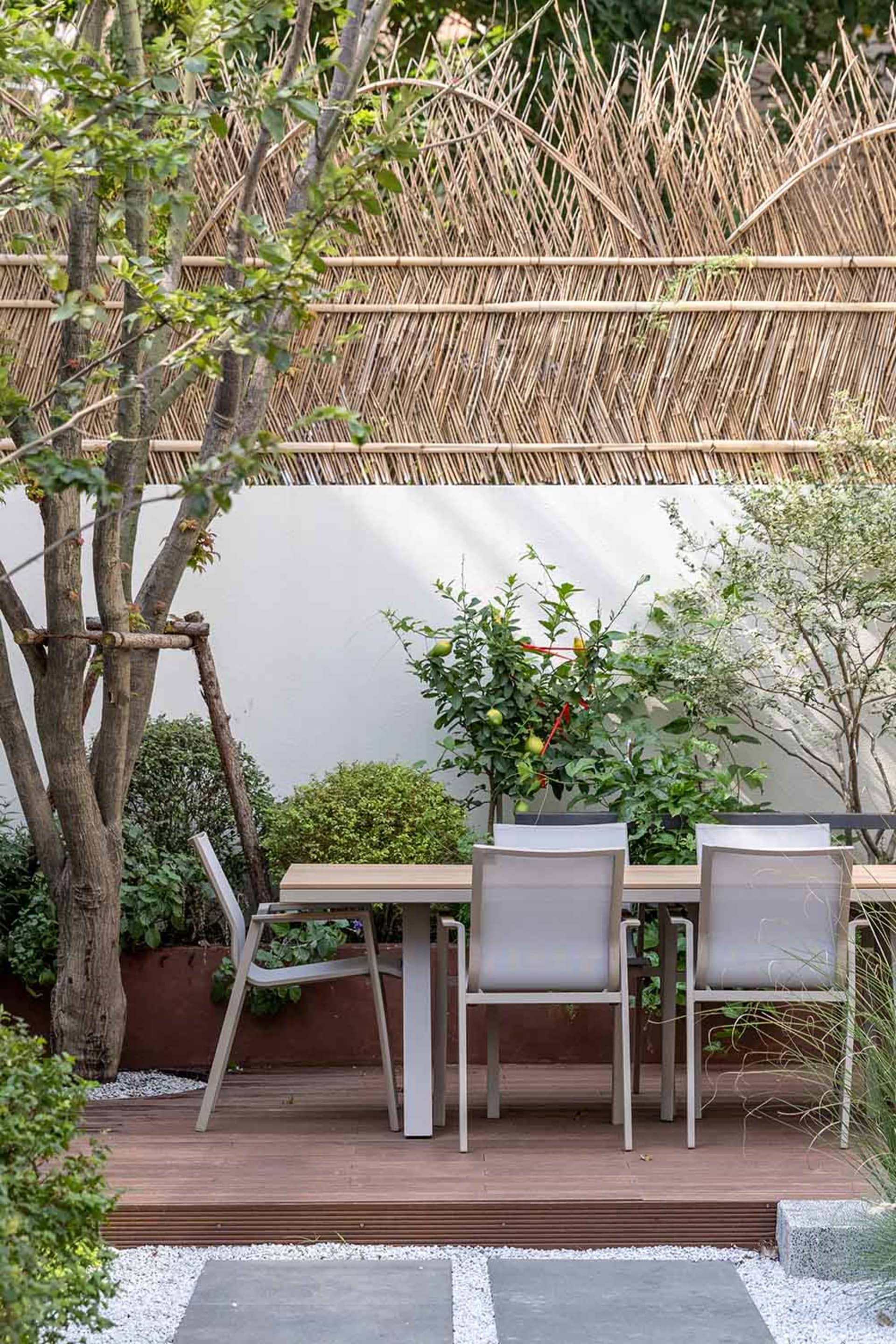 A modern wooden garden table with chairs surrounded by trees and plants.