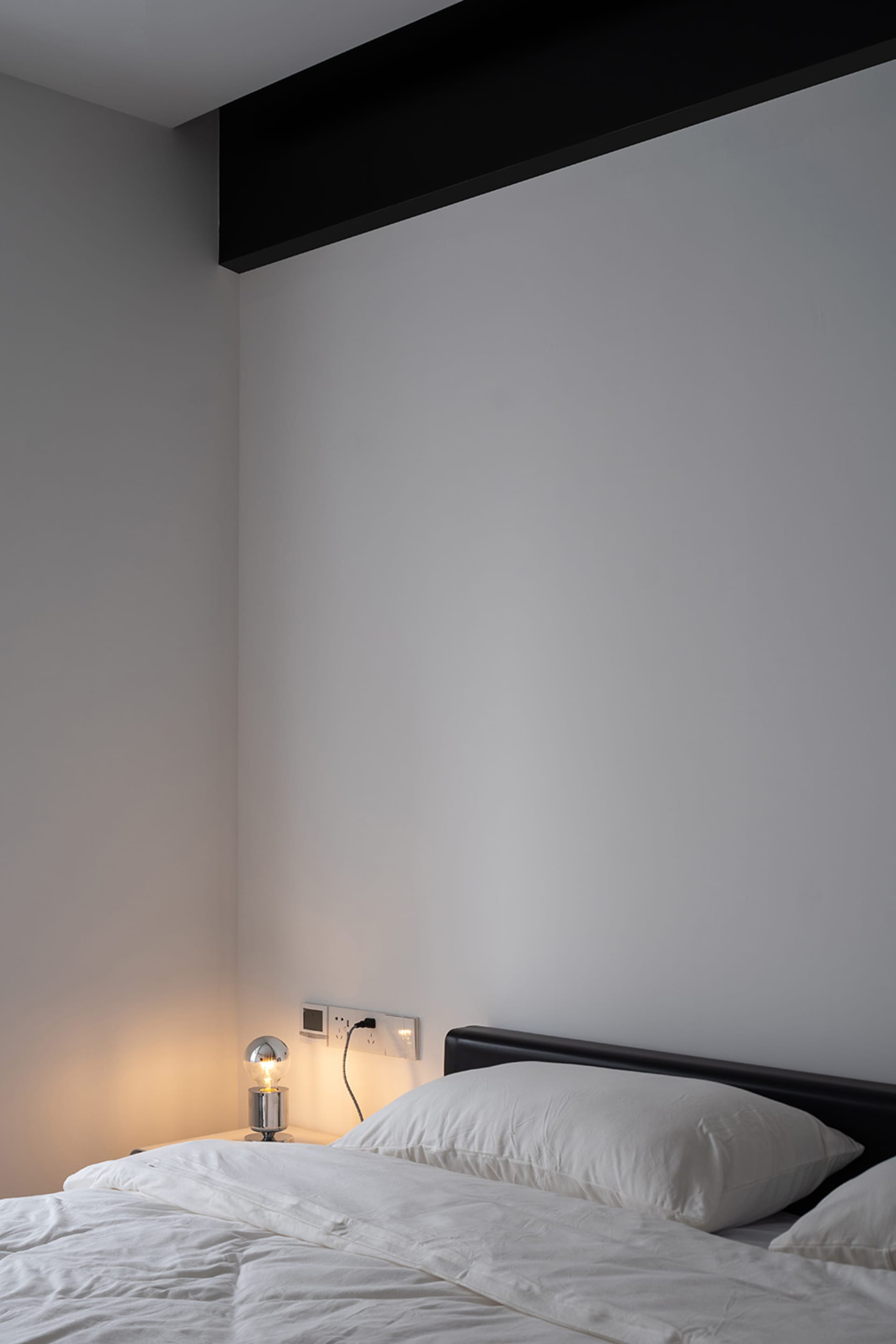 Minimalist bedroom with white pillows on an unmade bed, featuring a single light bulb on a bedside table.