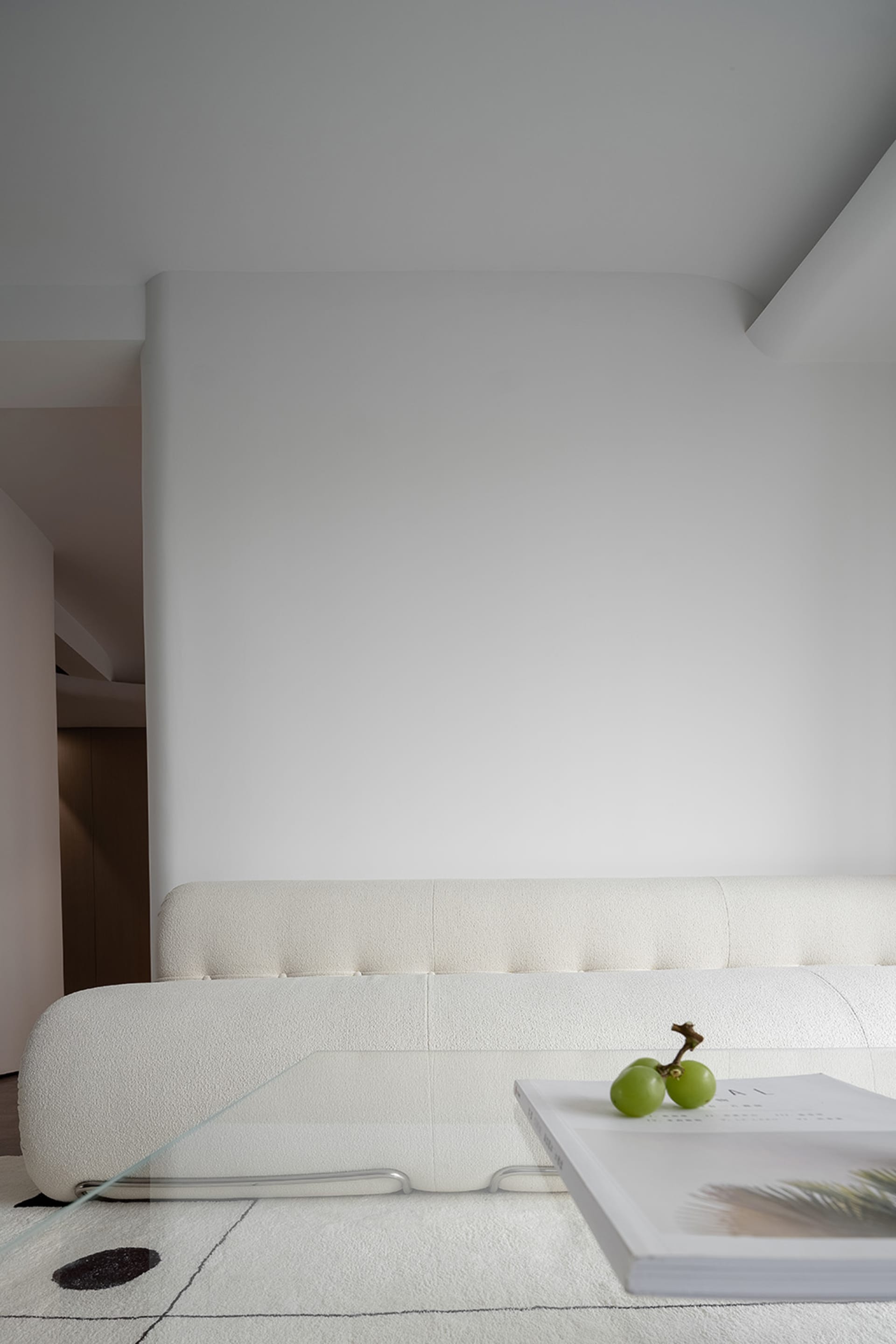 A modern white sofa lounge with a glass table displaying grapes and a book.