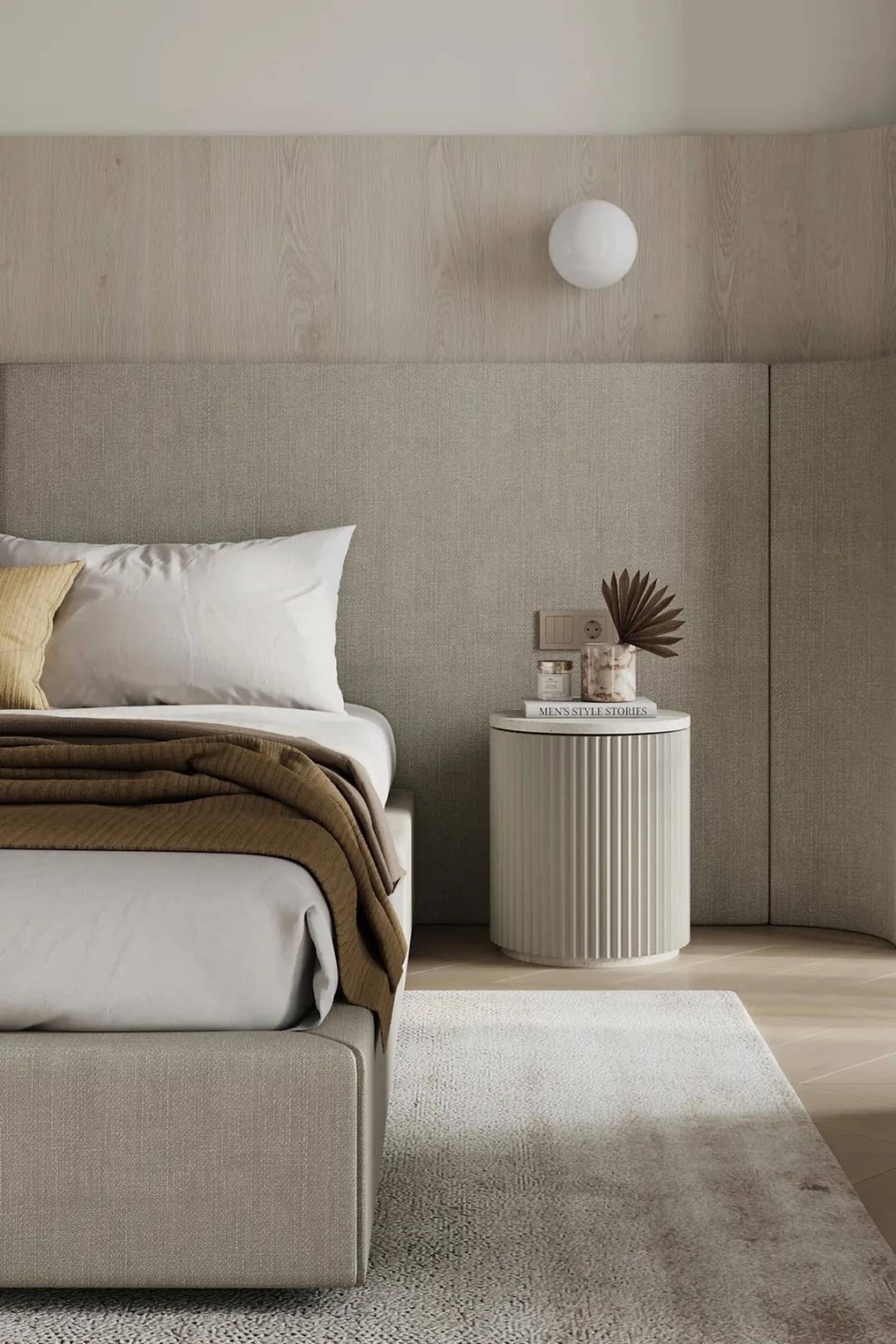 A modern minimalist bedroom with a fabric bed, wooden headboard, and a sleek, rounded bedside table with a marble top.