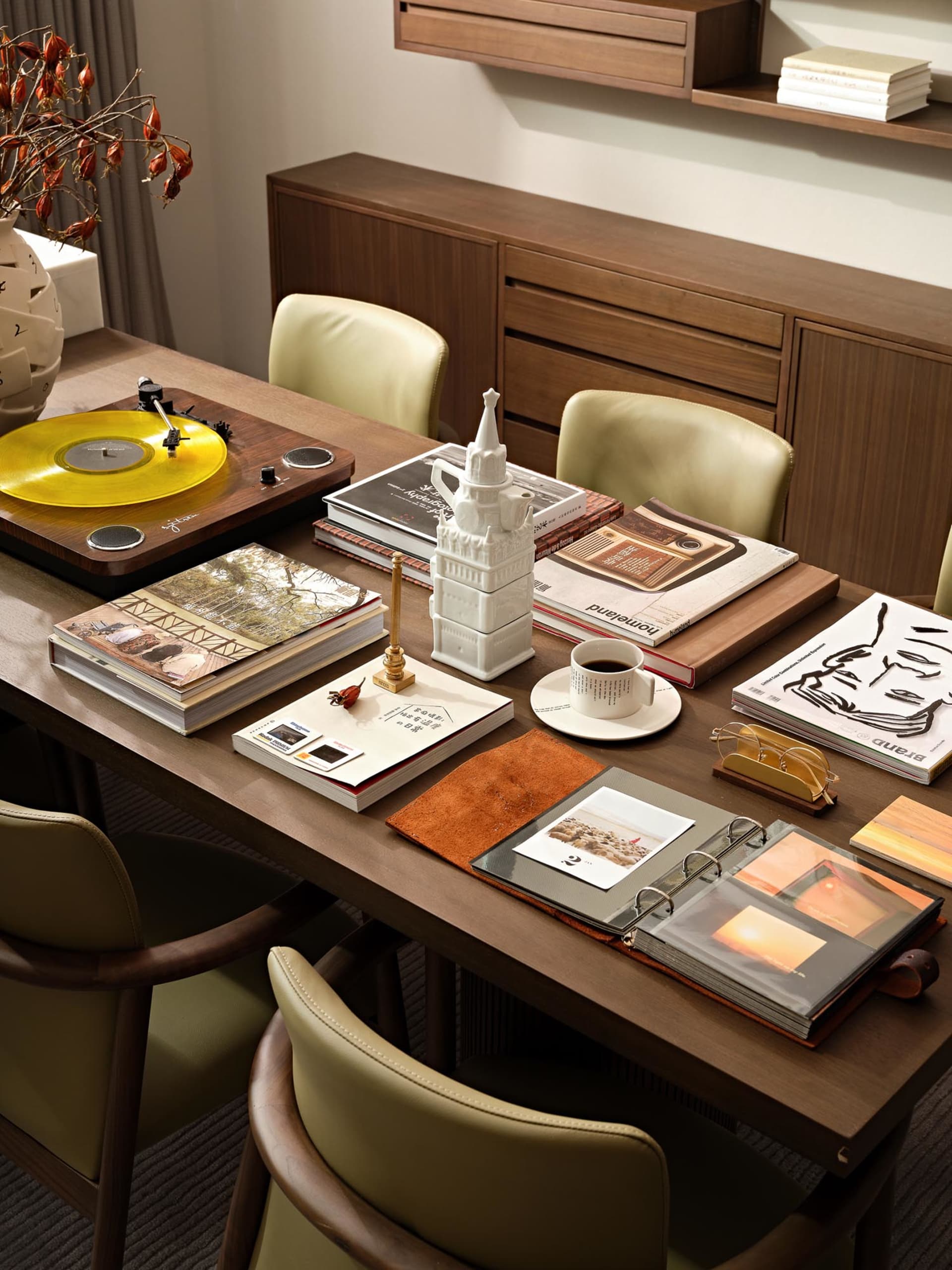 A modern interior design setting featuring a wooden table with books and a vinyl record player, with a vase of dried flowers