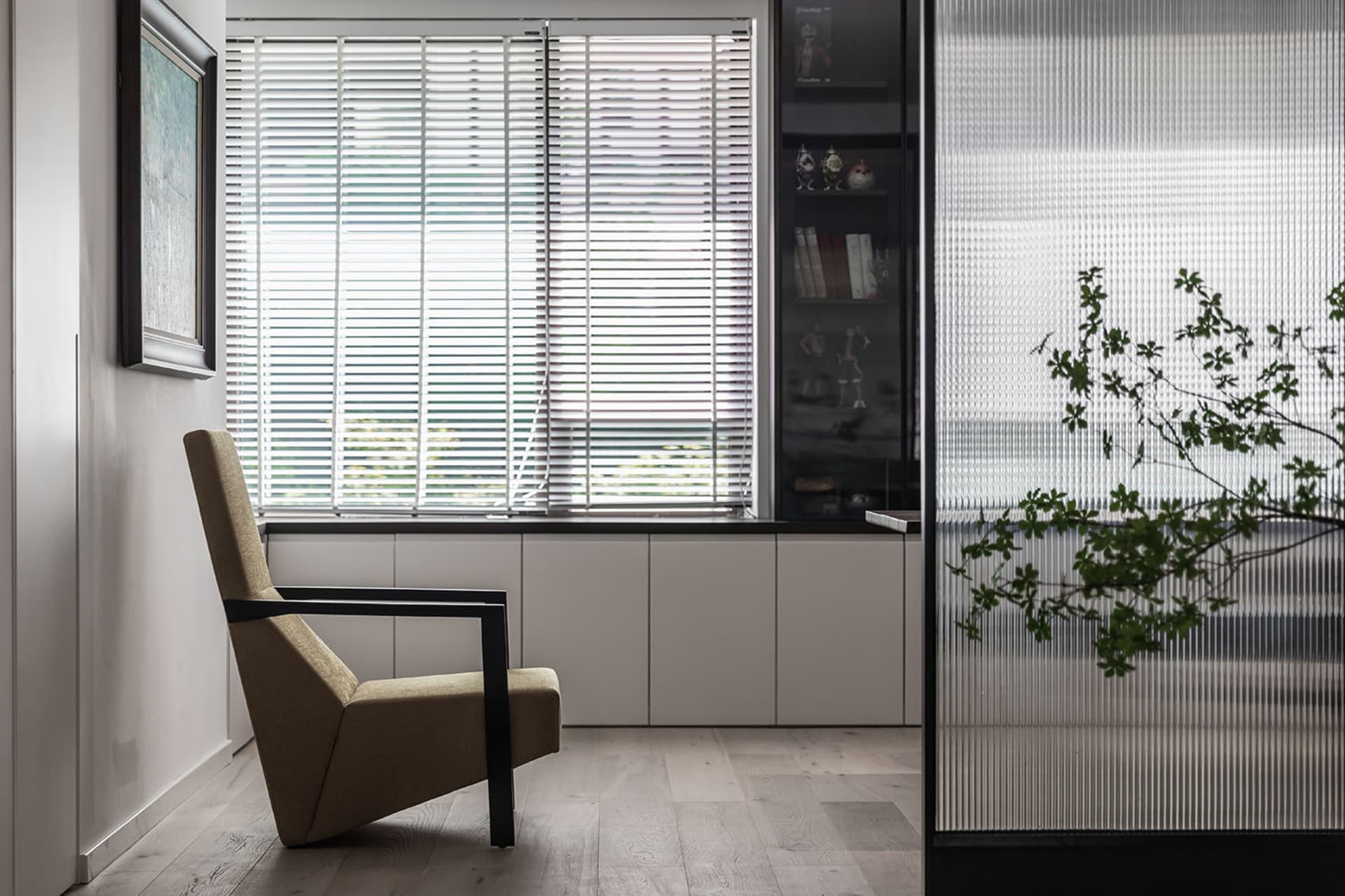 A modern living room featuring a comfortable chair, closed blinds, and a bookshelf with books and decorative items.