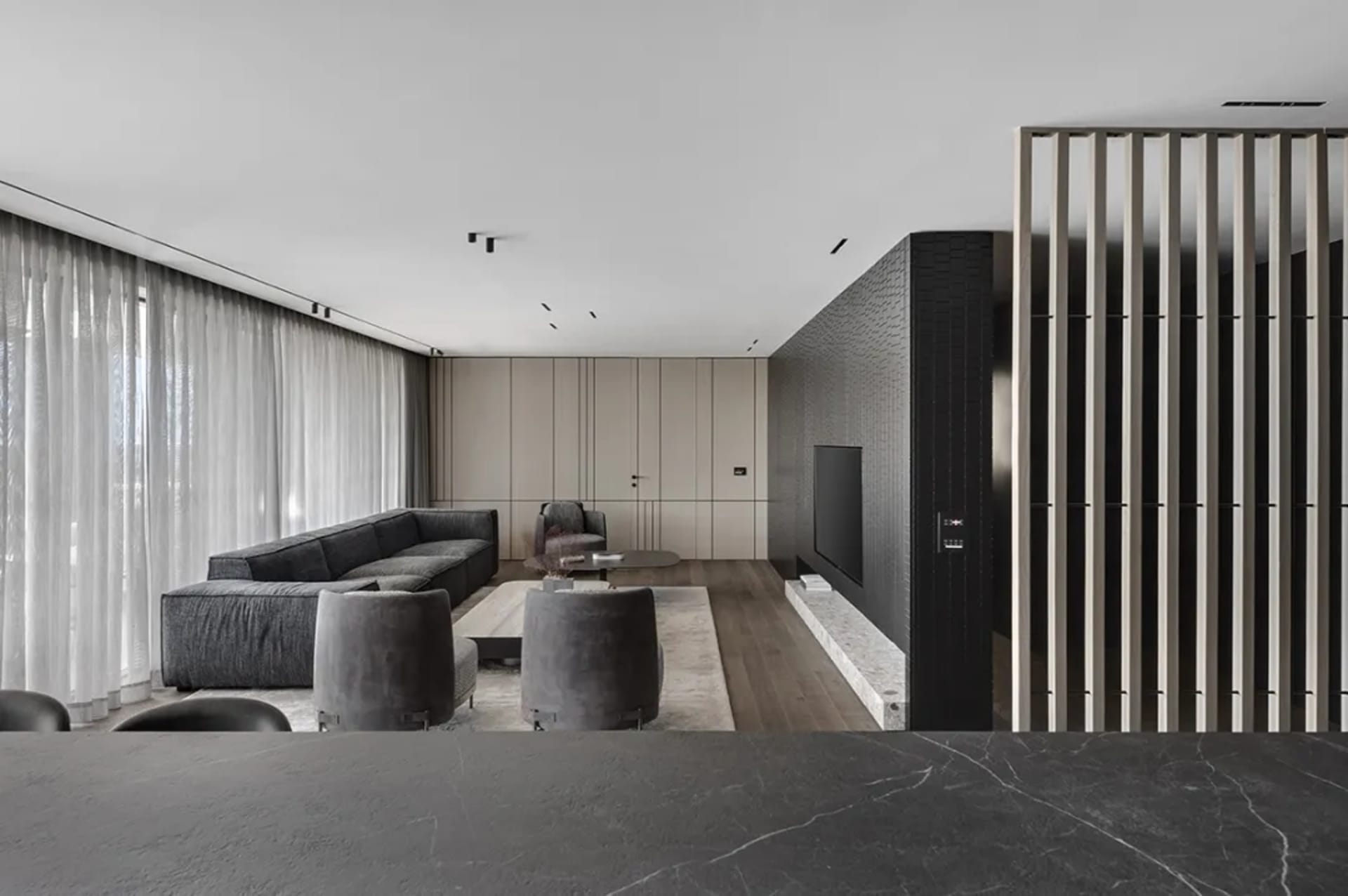 A modern, minimalist living room with dark wood flooring, light-colored walls, and mixed materials including leather furnitur