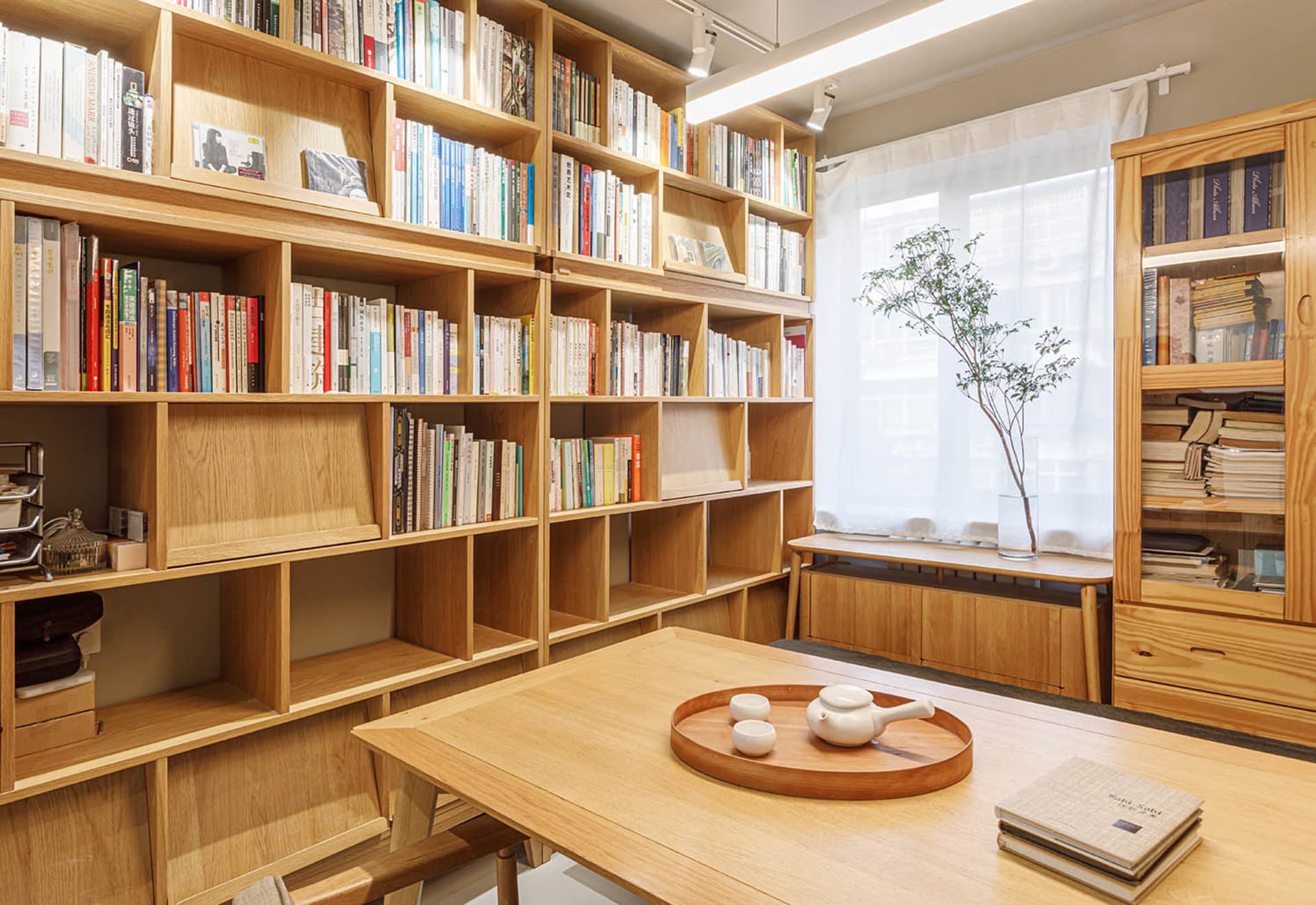 A modern living room featuring wooden shelves filled with books and a wooden table with a white teapot and two cups.