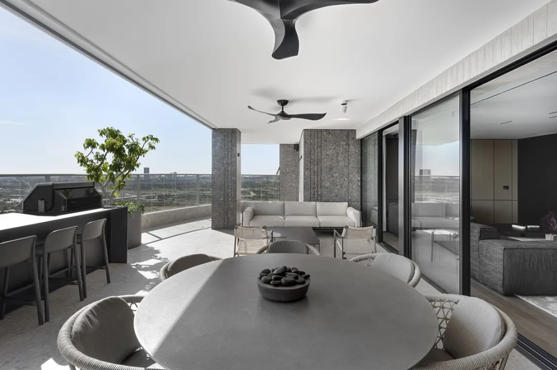 Modern living space with concrete walls, large windows, and a dining area with round table and chairs.