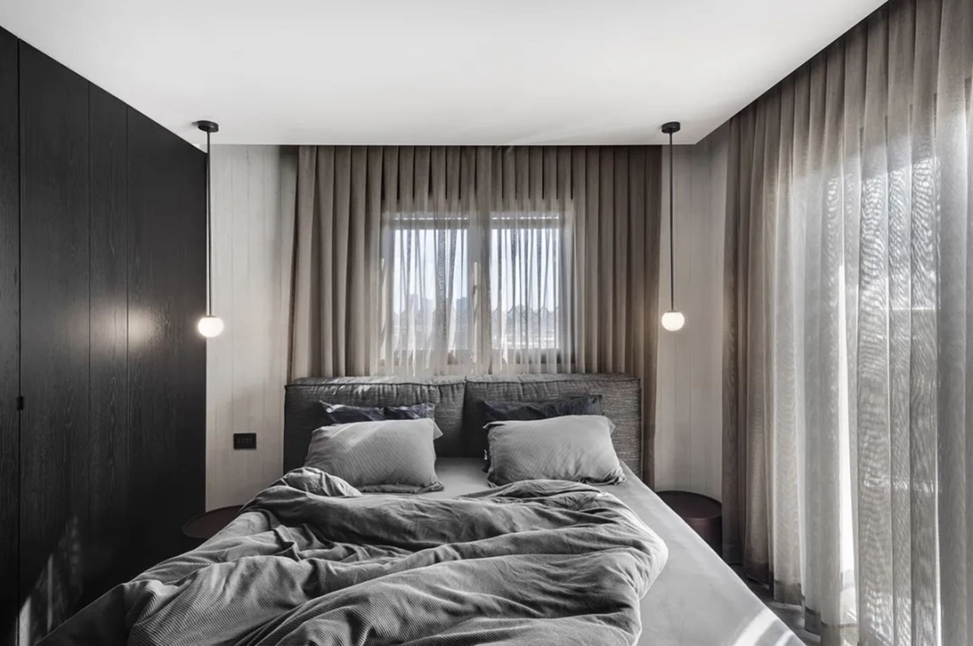 A modern minimalist bedroom with a textured bed, neatly arranged pillows, and sheer curtains.