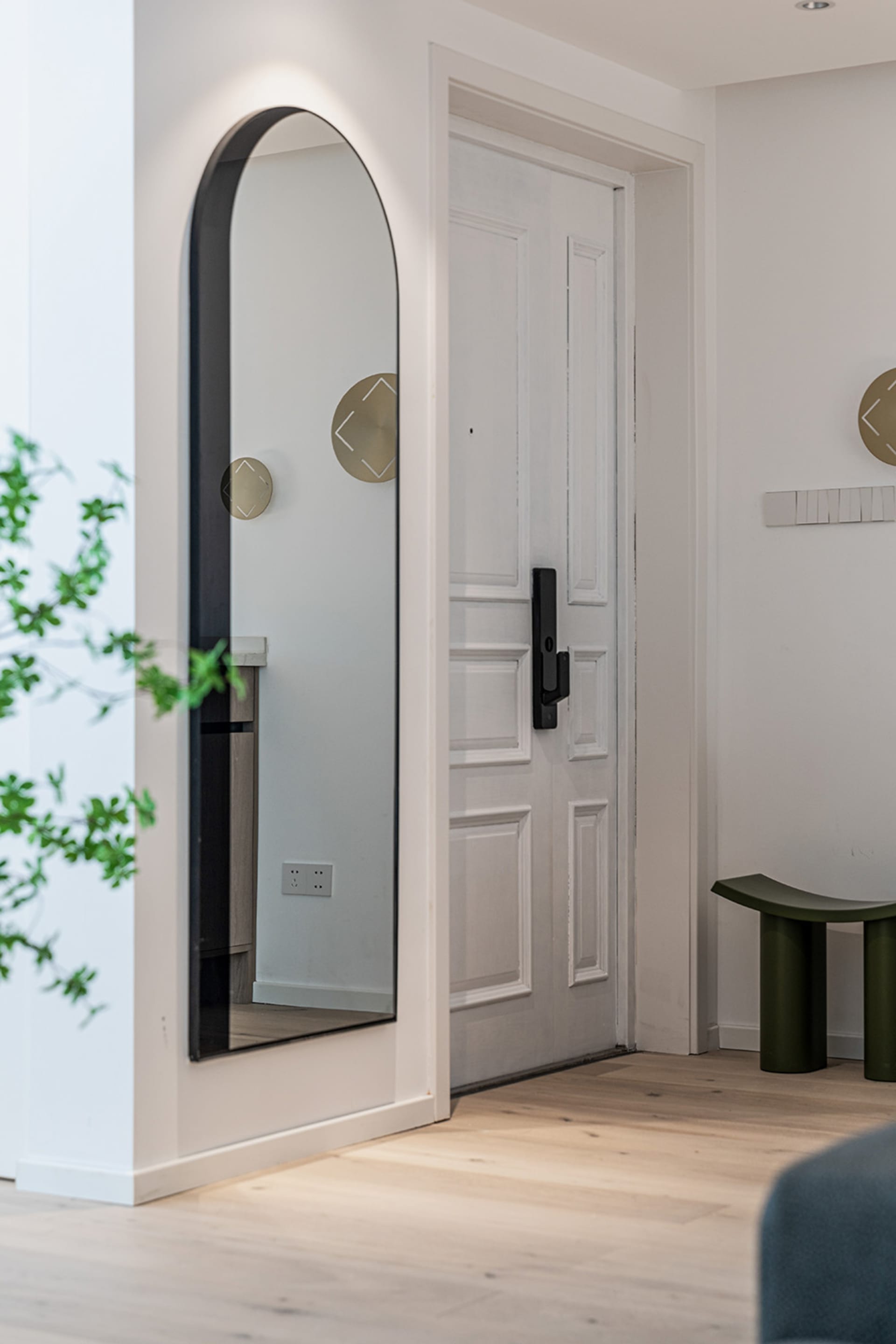 A white entrance hall featuring a large, framed mirror with an arched top on the left side, a white paneled door on the right