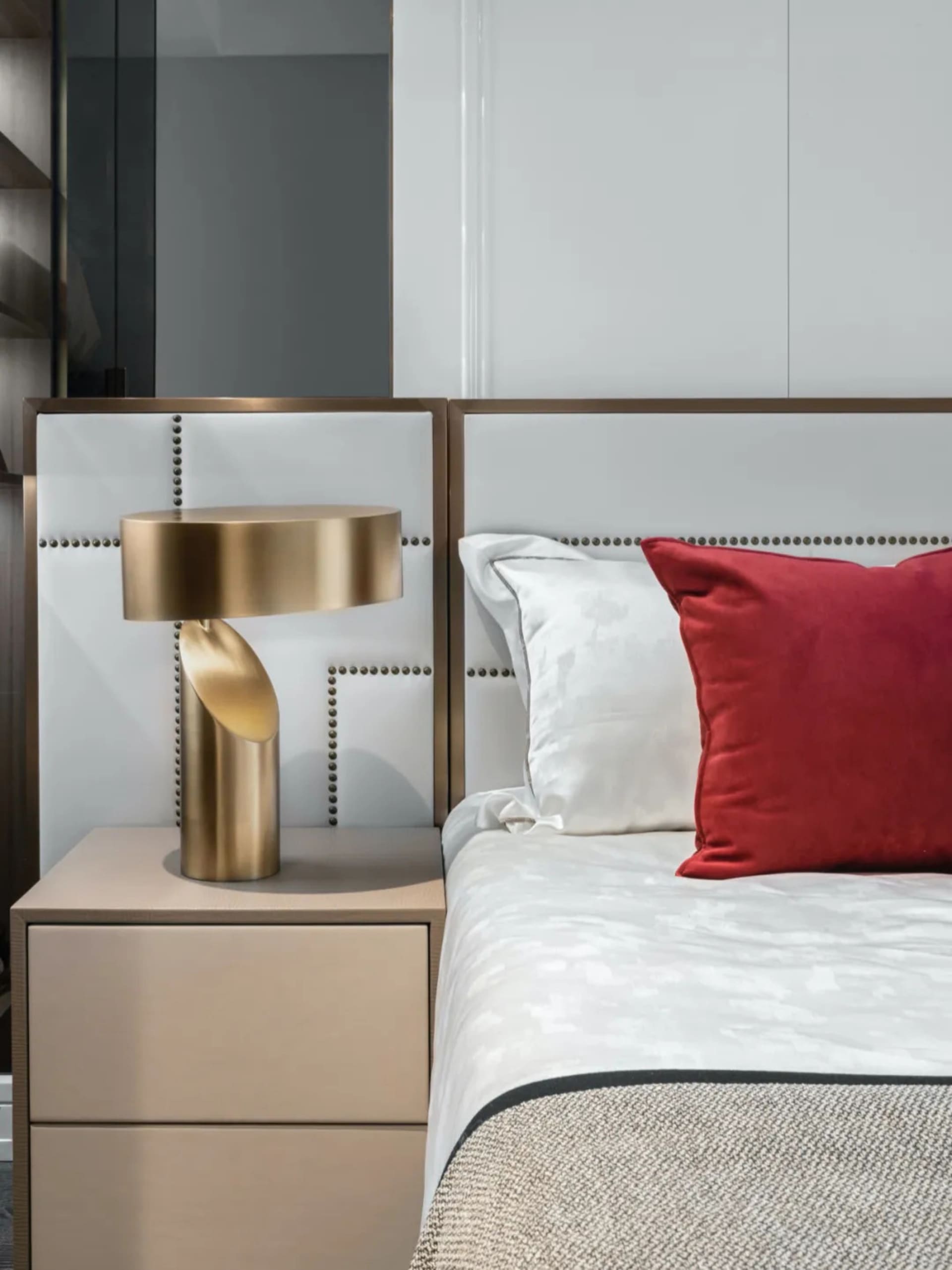 A modern bedroom with a white leather headboard adorned with gold accents and a red decorative pillow, featuring an arc lamp