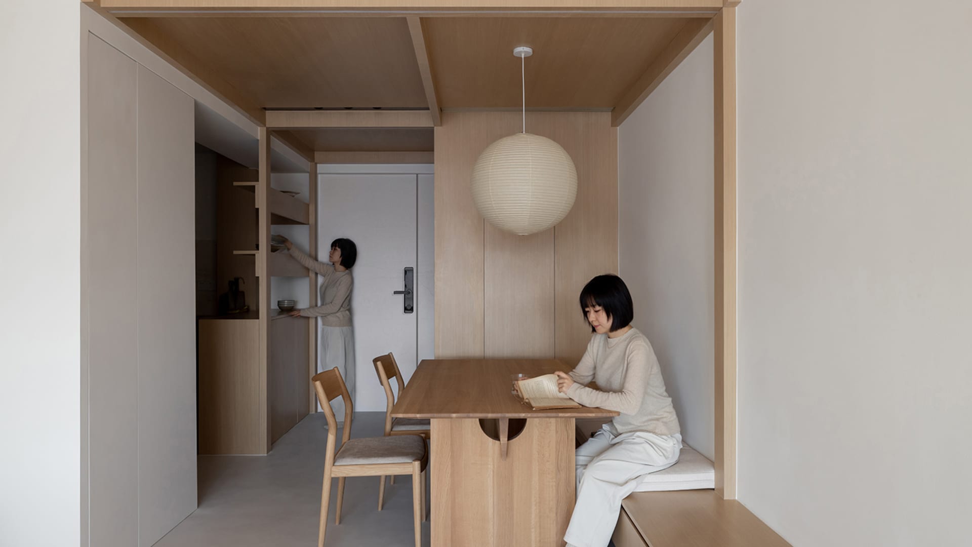人物坐在簡約餐廳區,搭配木質家具與圓形燈具。