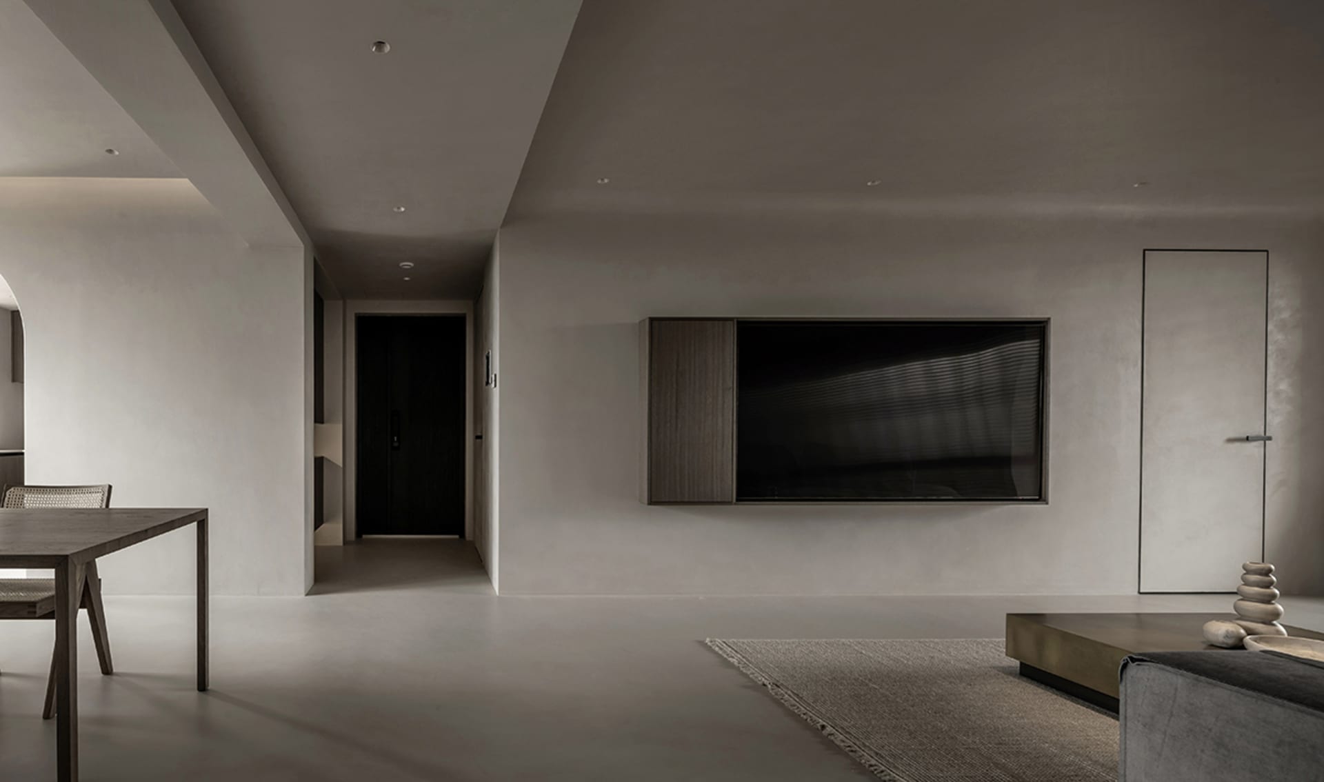 A modern minimalist living room with a concrete floor, dark wood furniture, and a large TV mounted on the wall.