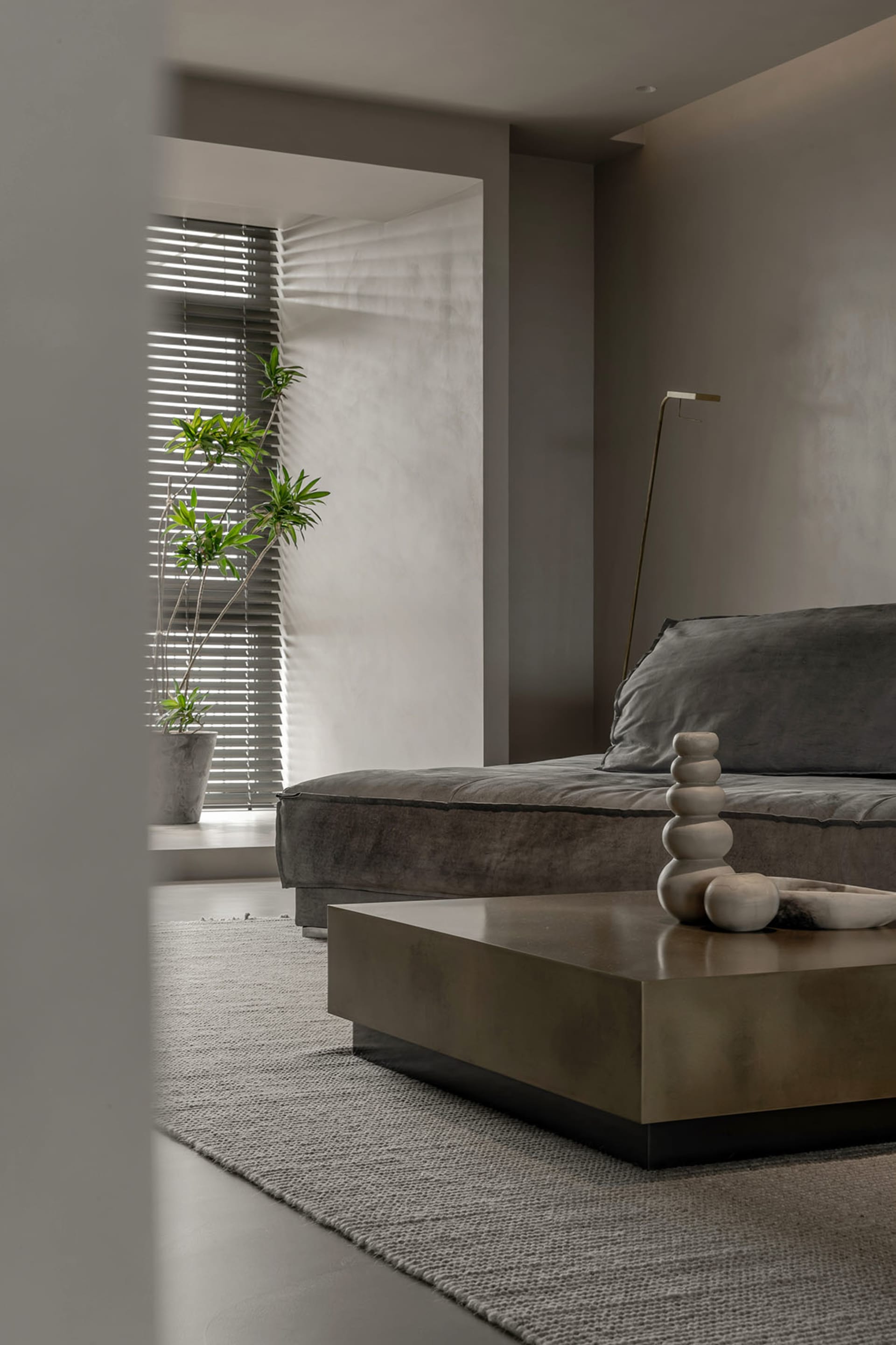 A modern living room with a minimalist design featuring a concrete coffee table and a gray couch with a vase of plants.