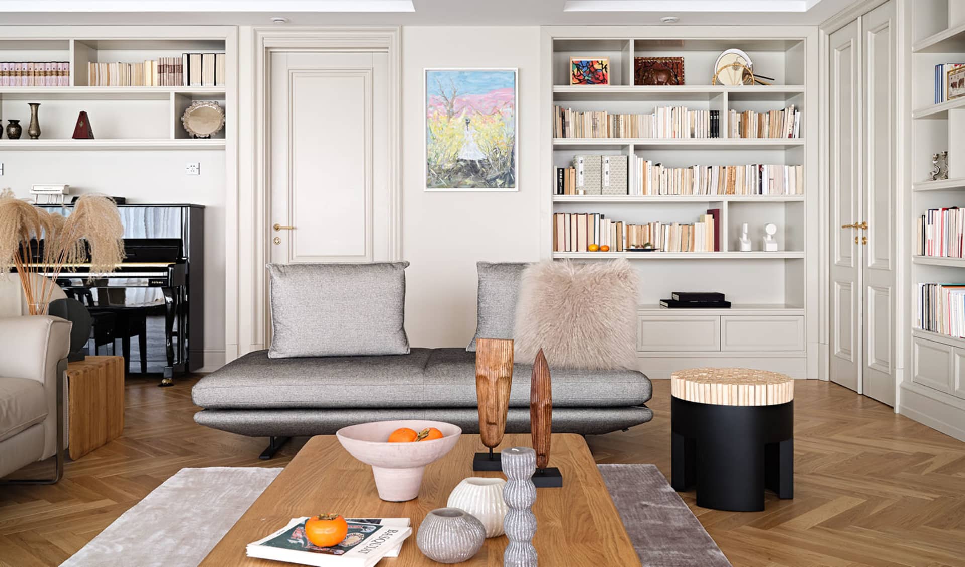 A modern living room with neutral-toned furniture, wooden floor, and bookshelves filled with books.