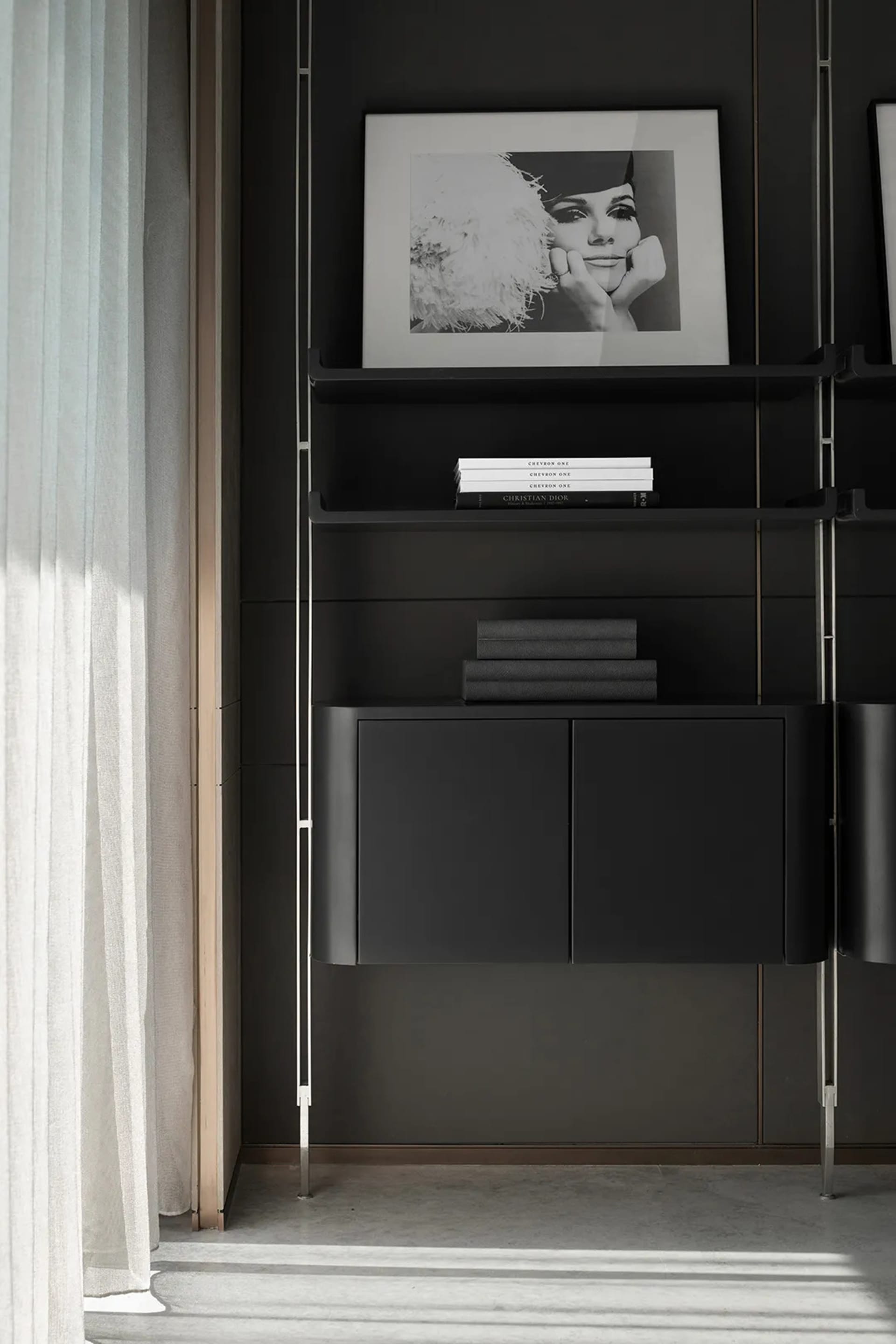 A modern black metal shelf with books and a framed black and white portrait of a woman.