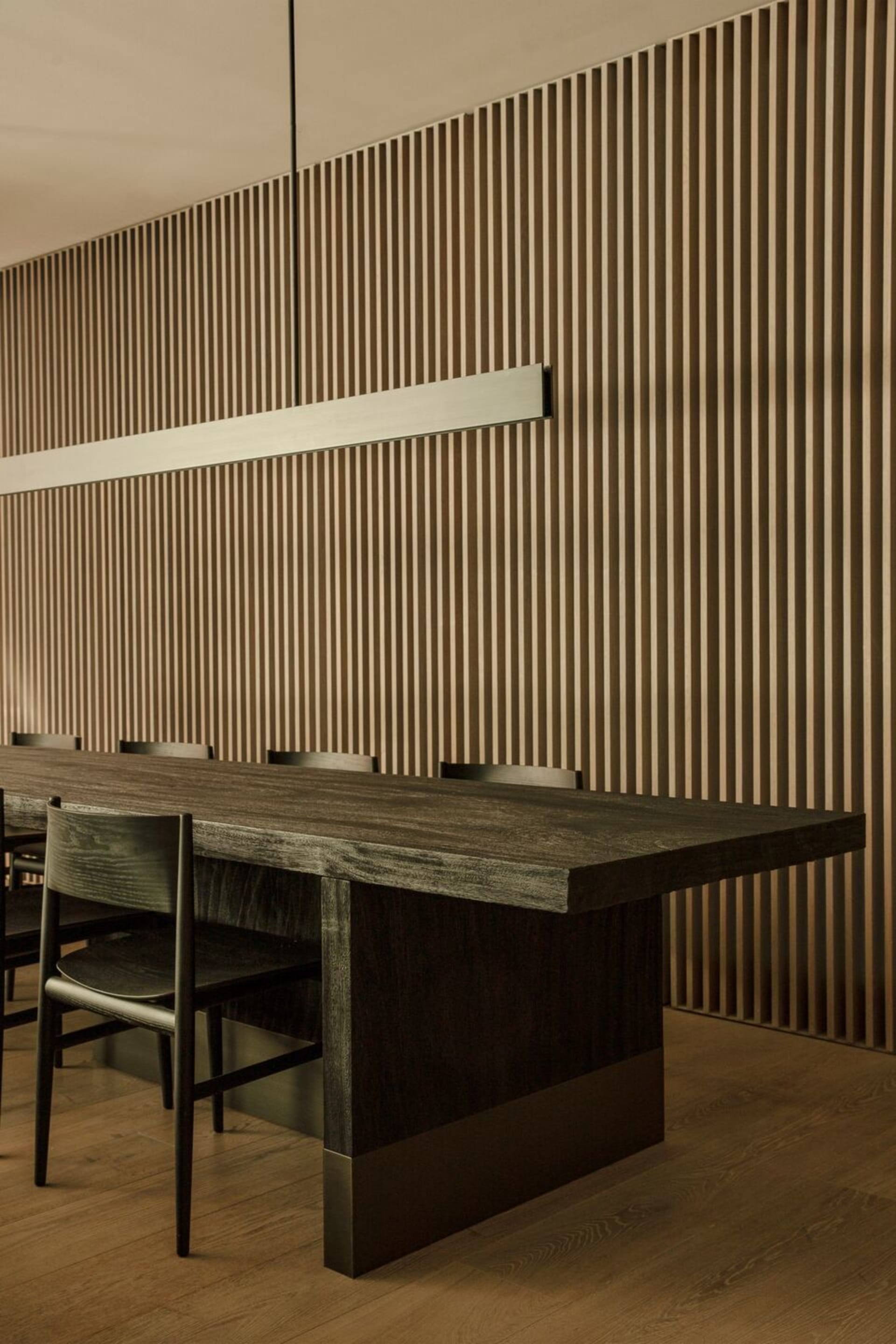 Modern minimalist restaurant interior featuring a wooden table and chairs against a wooden panel wall.