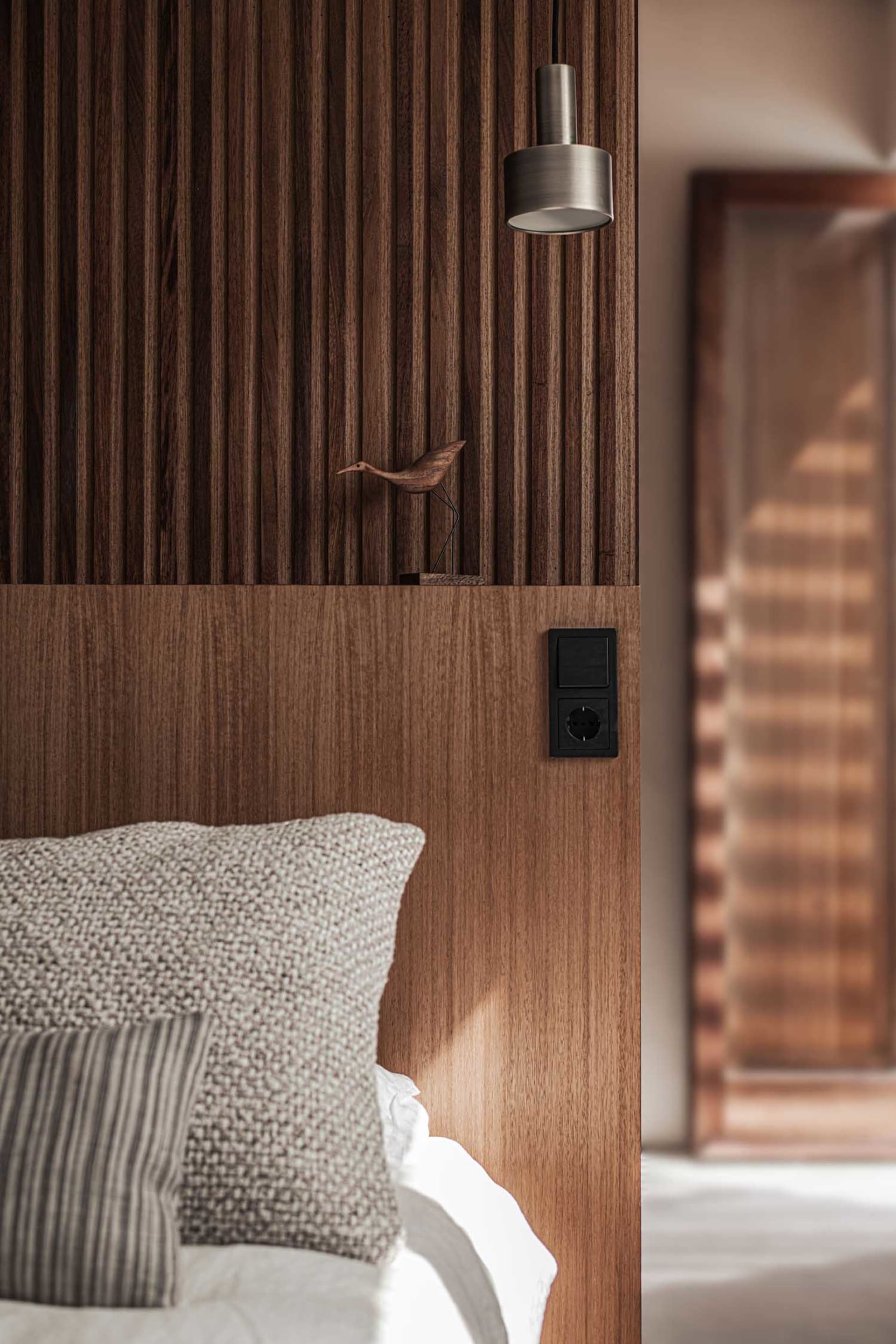 Modern, minimalist bedroom featuring a wooden headboard with a small bird sculpture on top.