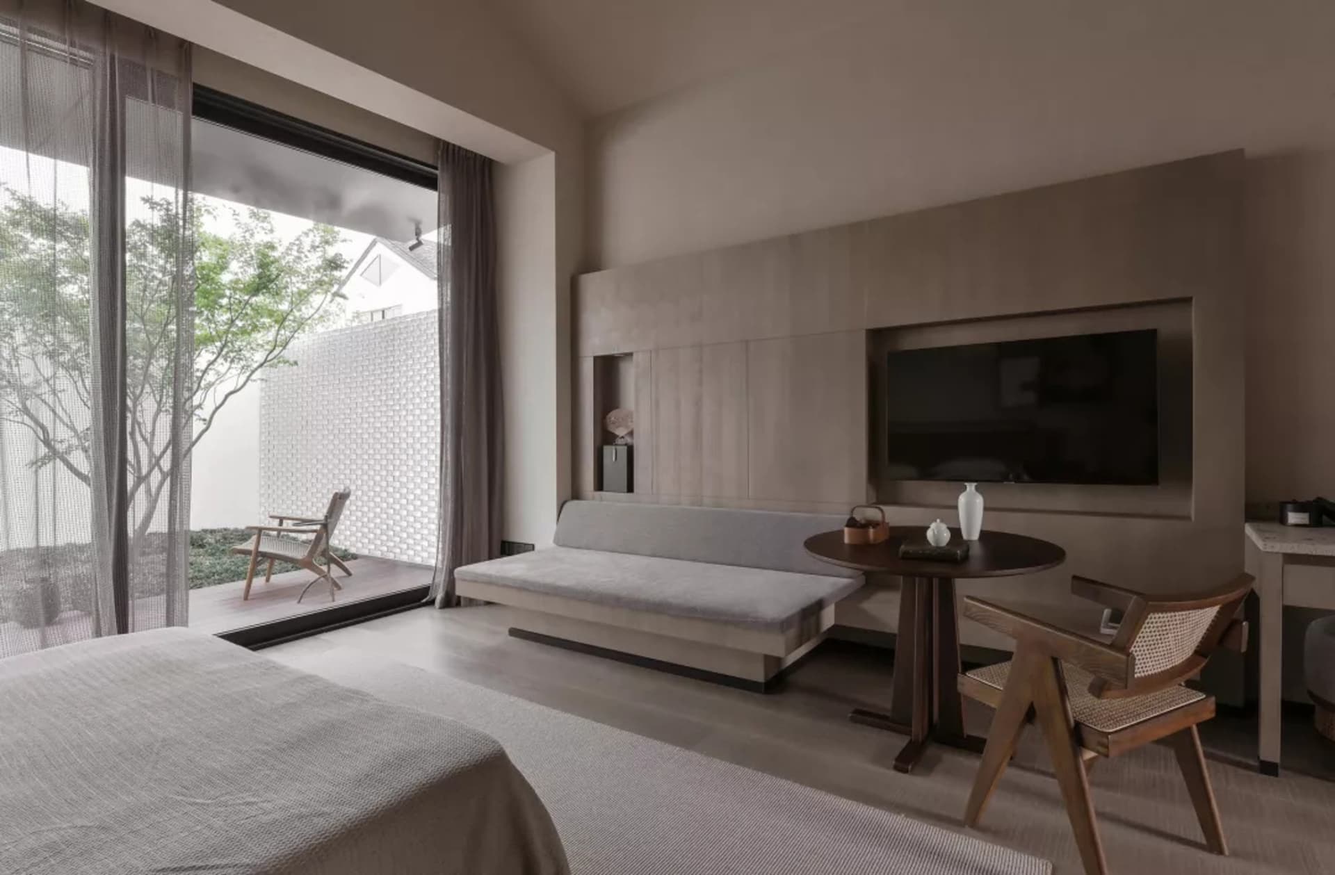 A minimalist bedroom with neutral-toned furniture and a large window overlooking greenery.