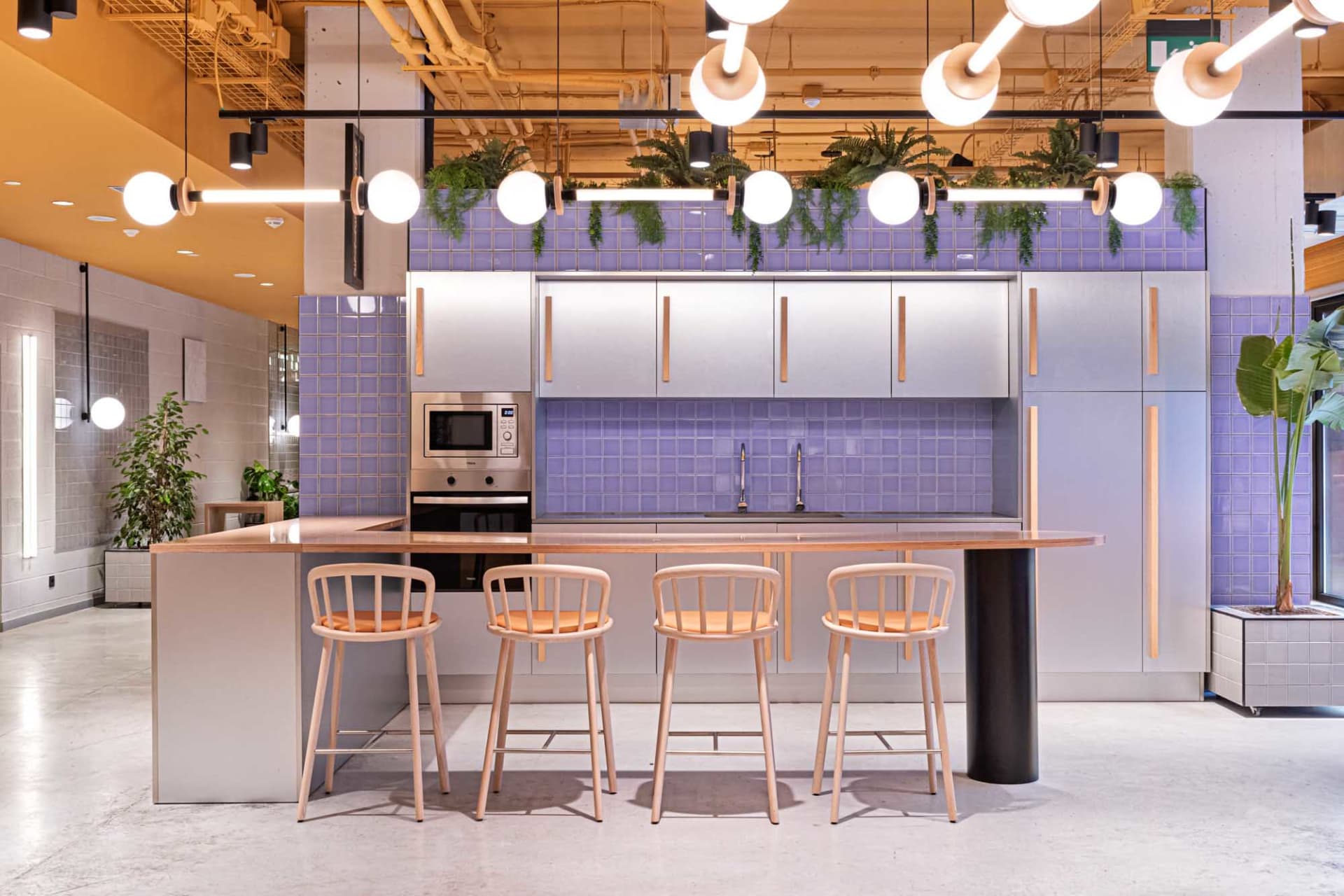 A minimalist commercial kitchen with wooden stools, metal cabinets, and glass tiles.