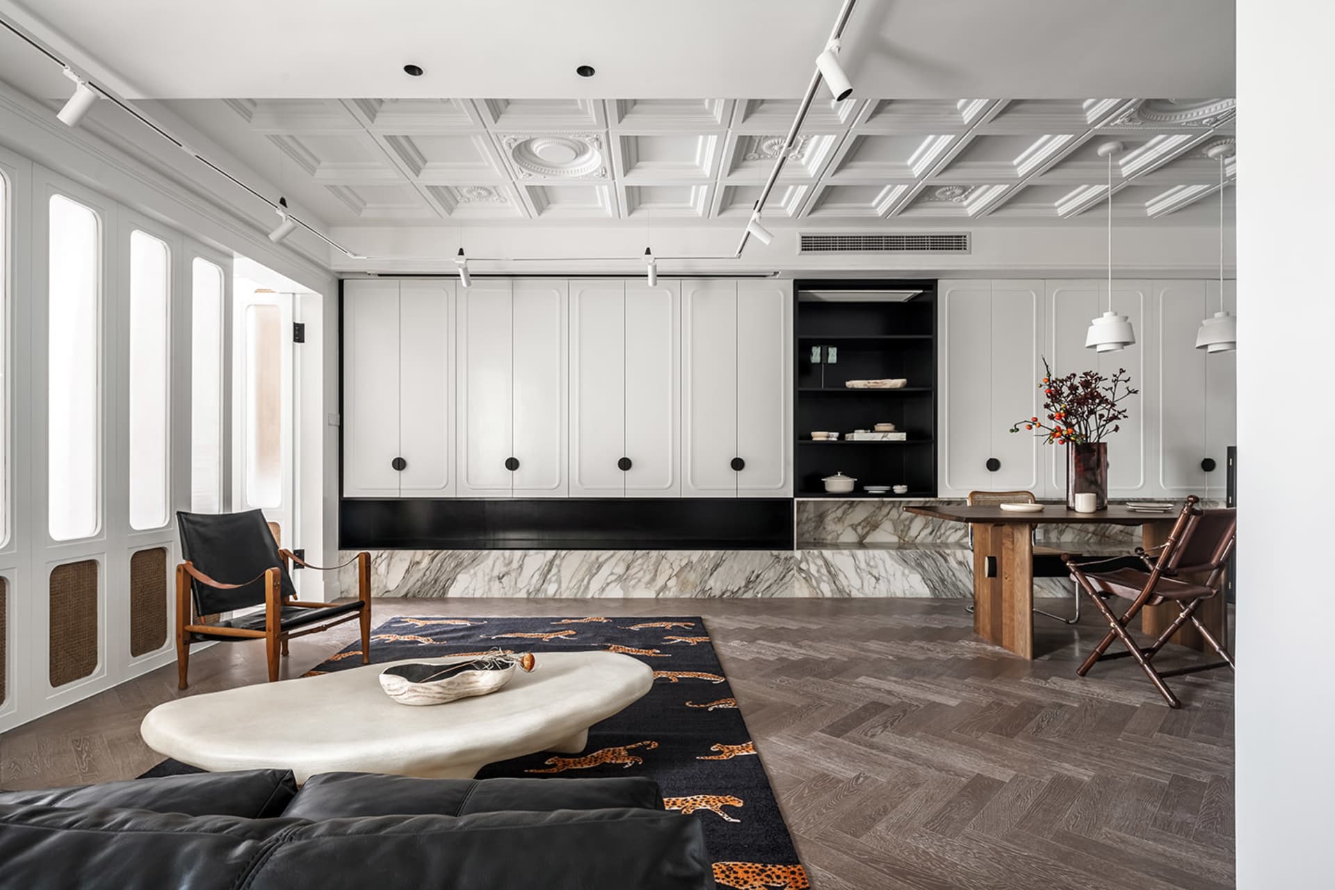 A minimalist living room with white marble accents and a black leather sofa on a black and orange leopard print rug, set agai