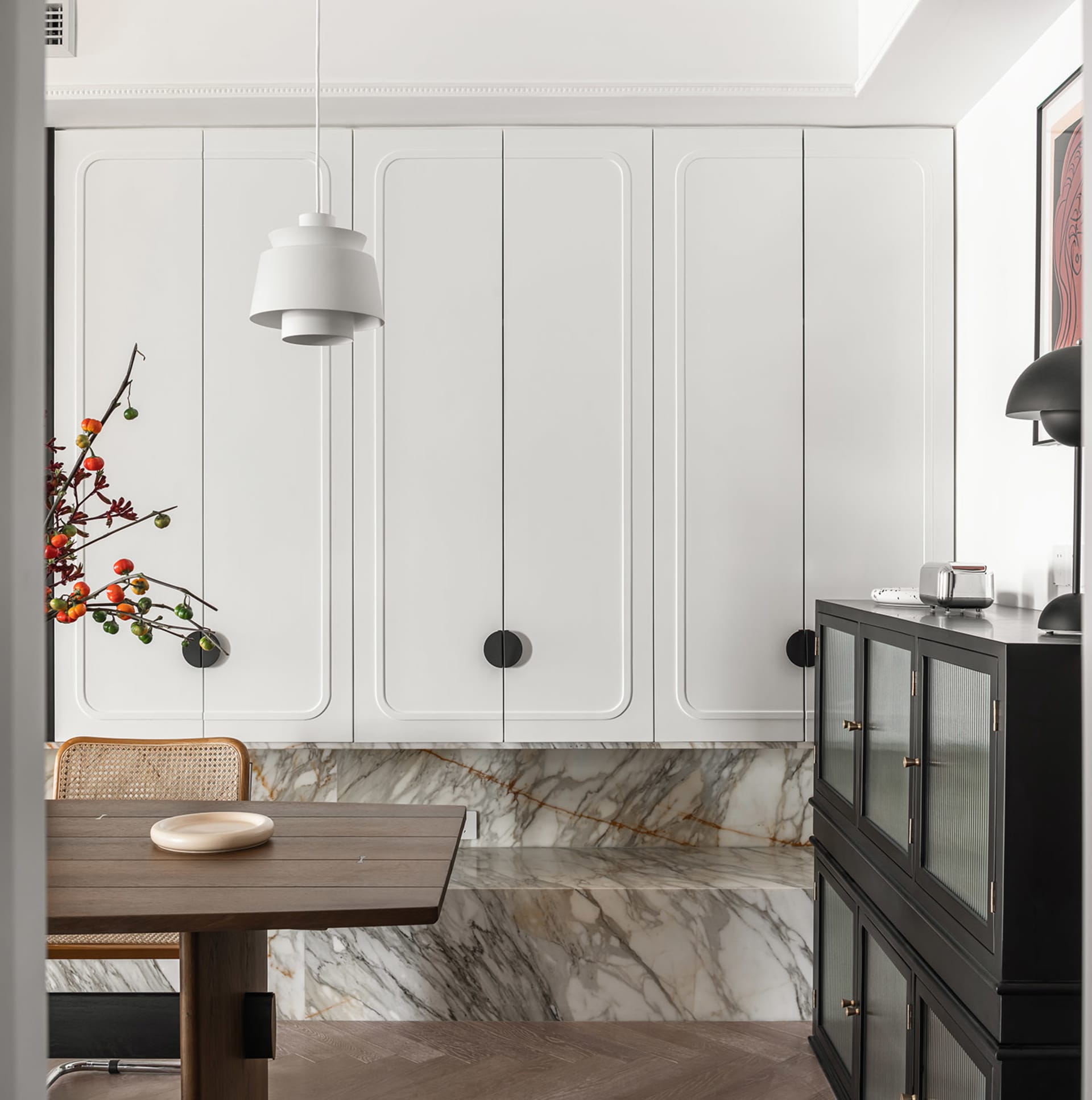 A modern kitchen with white cabinets, marble backsplash, and a wooden dining table.