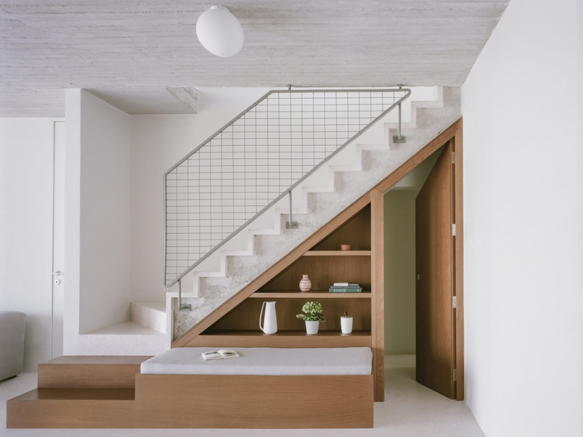 A minimalist house features a concrete staircase with a white railing and a wooden bench seat.