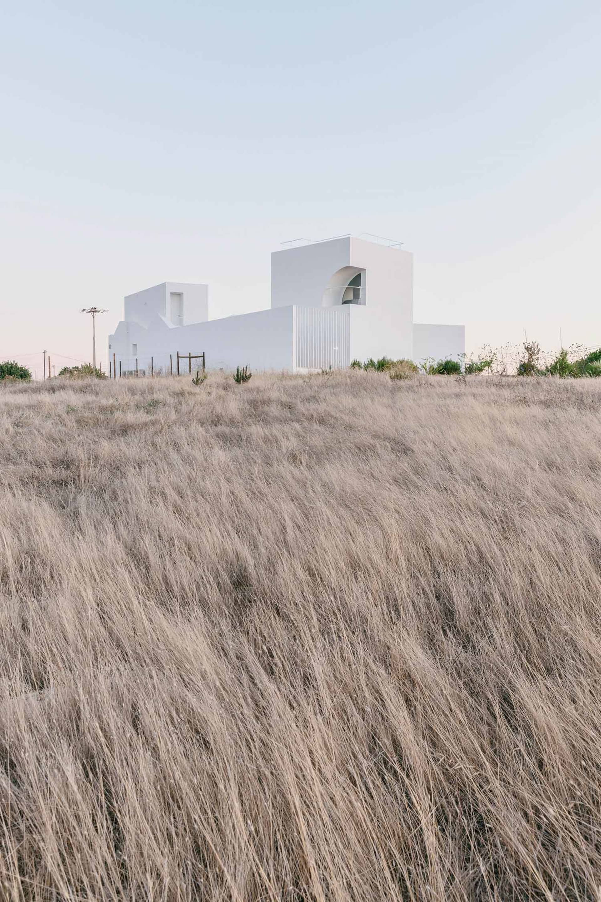 A minimalist white house surrounded by dry grass in a canyon landscape.