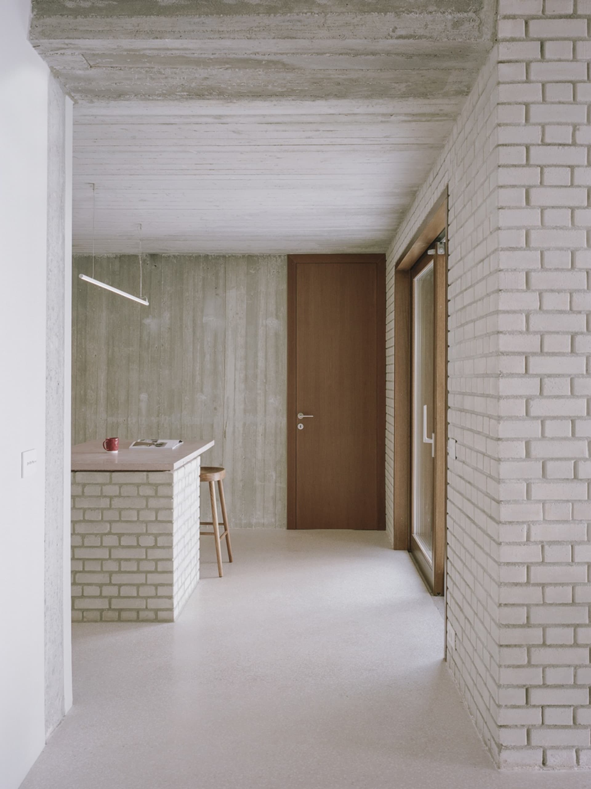 A modern minimalist kitchen with concrete walls, a wooden countertop, and a wooden stool.