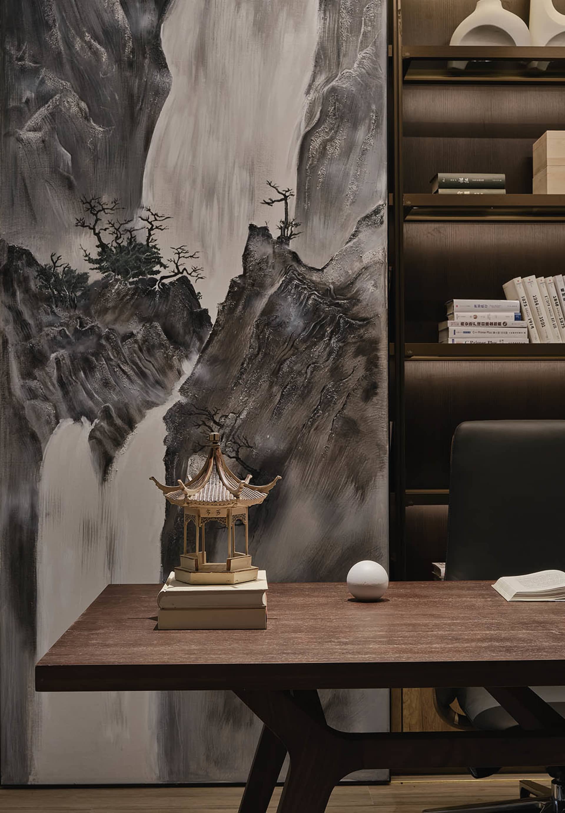 A modern office desk with a wooden top and a minimalist design sits in front of a mural depicting a mountain landscape. The d