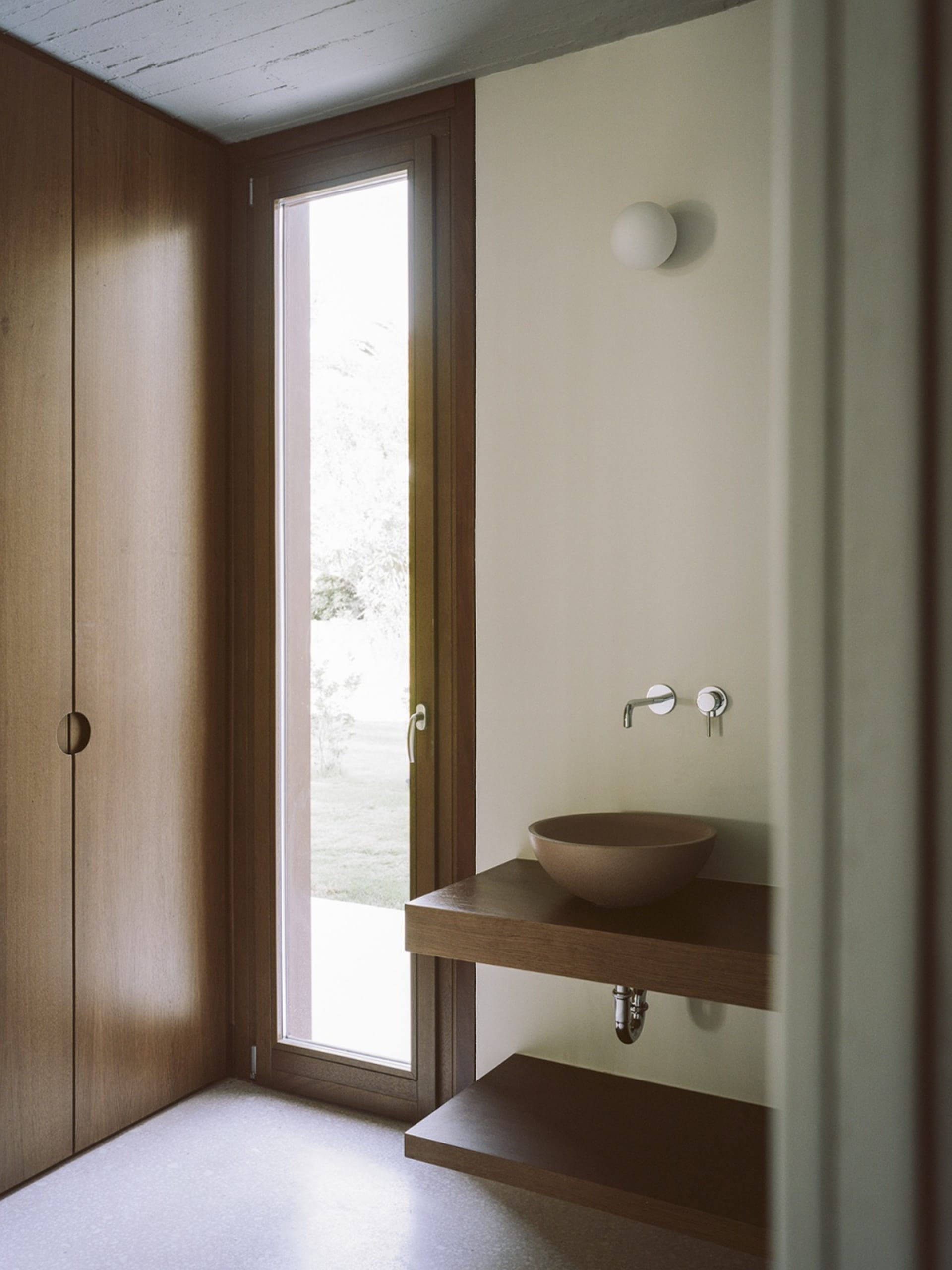 A minimalist bathroom with wooden elements, featuring a small sink and a large window.