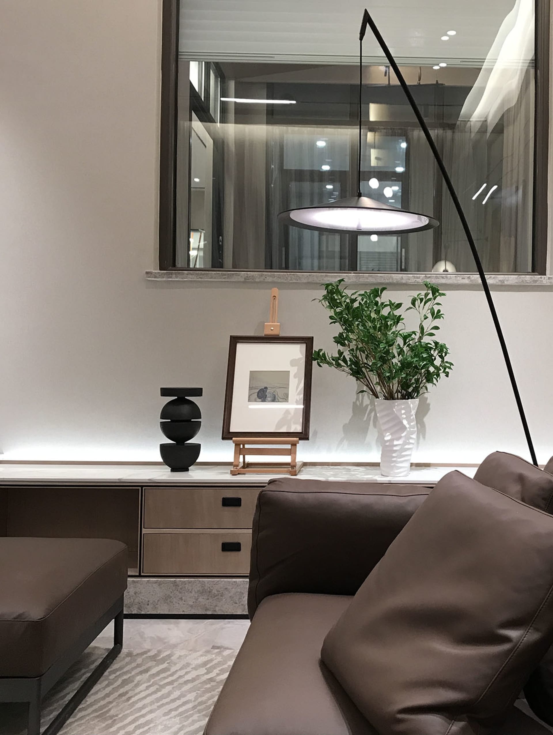 現代客廳內擺放棕色皮革沙發、吊燈,以及木質層架上的植物。