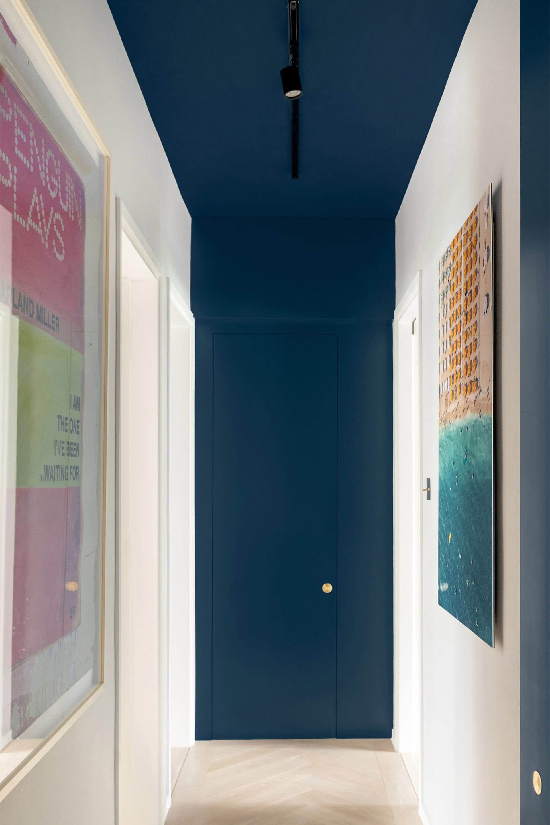 A hallway with navy blue walls and white doors, featuring framed colorful artworks on the walls.