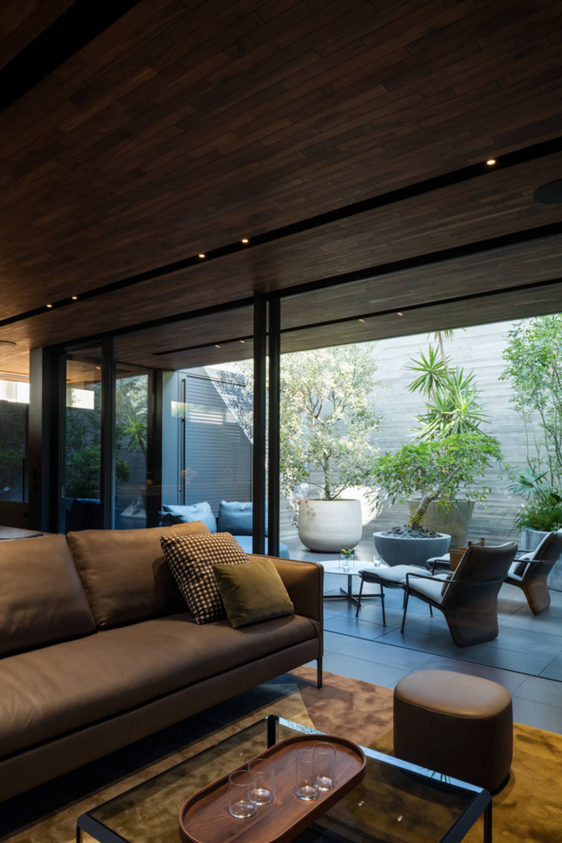 A minimalist living room featuring wood-paneled walls, a glass coffee table, and a brown leather sofa.