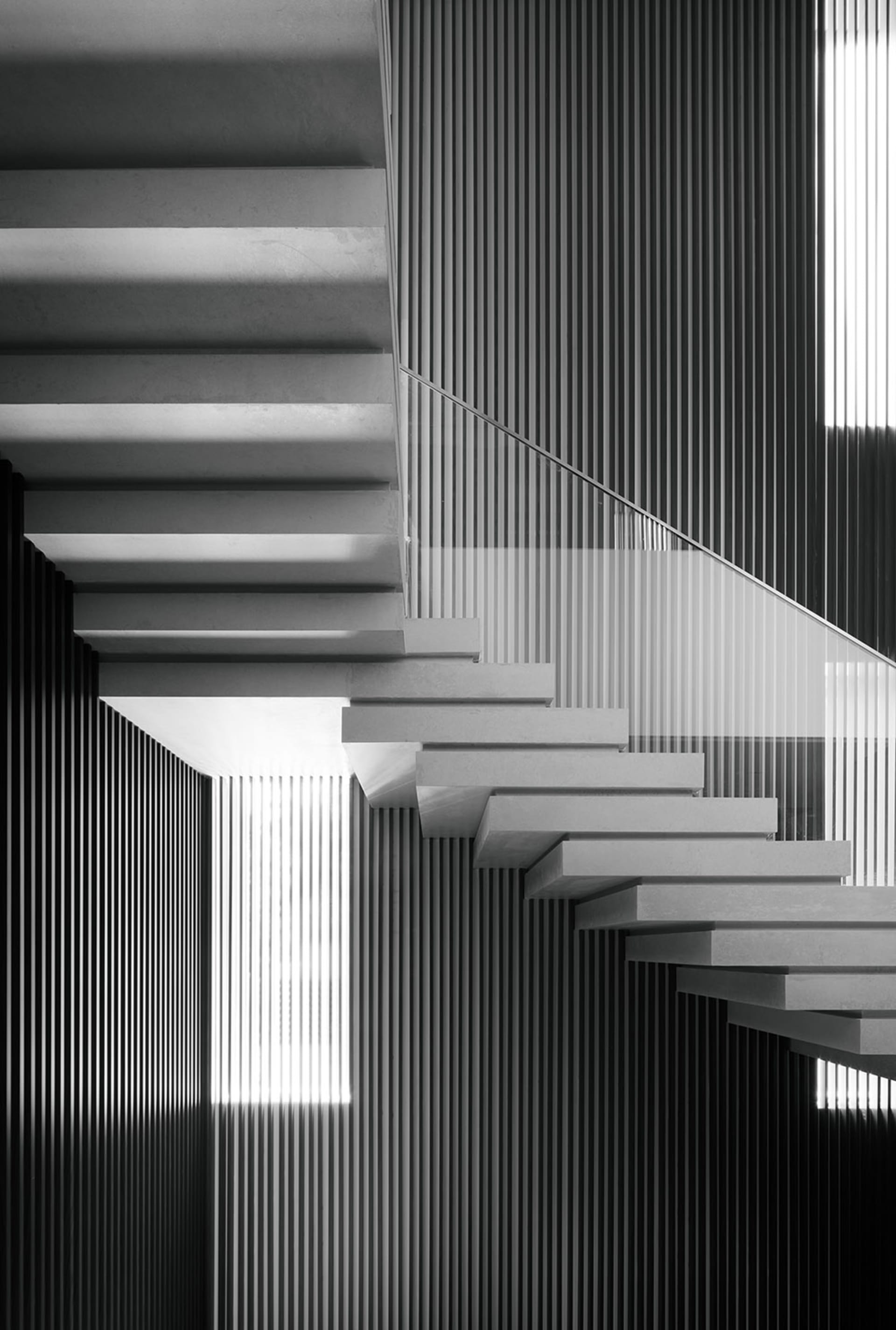 A modern staircase made of concrete with a glass railing against a wall of vertical lines.