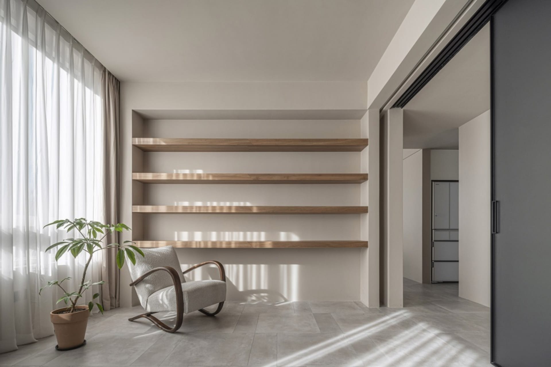 A modern living room with wooden shelves, a gray armchair, and a potted plant.