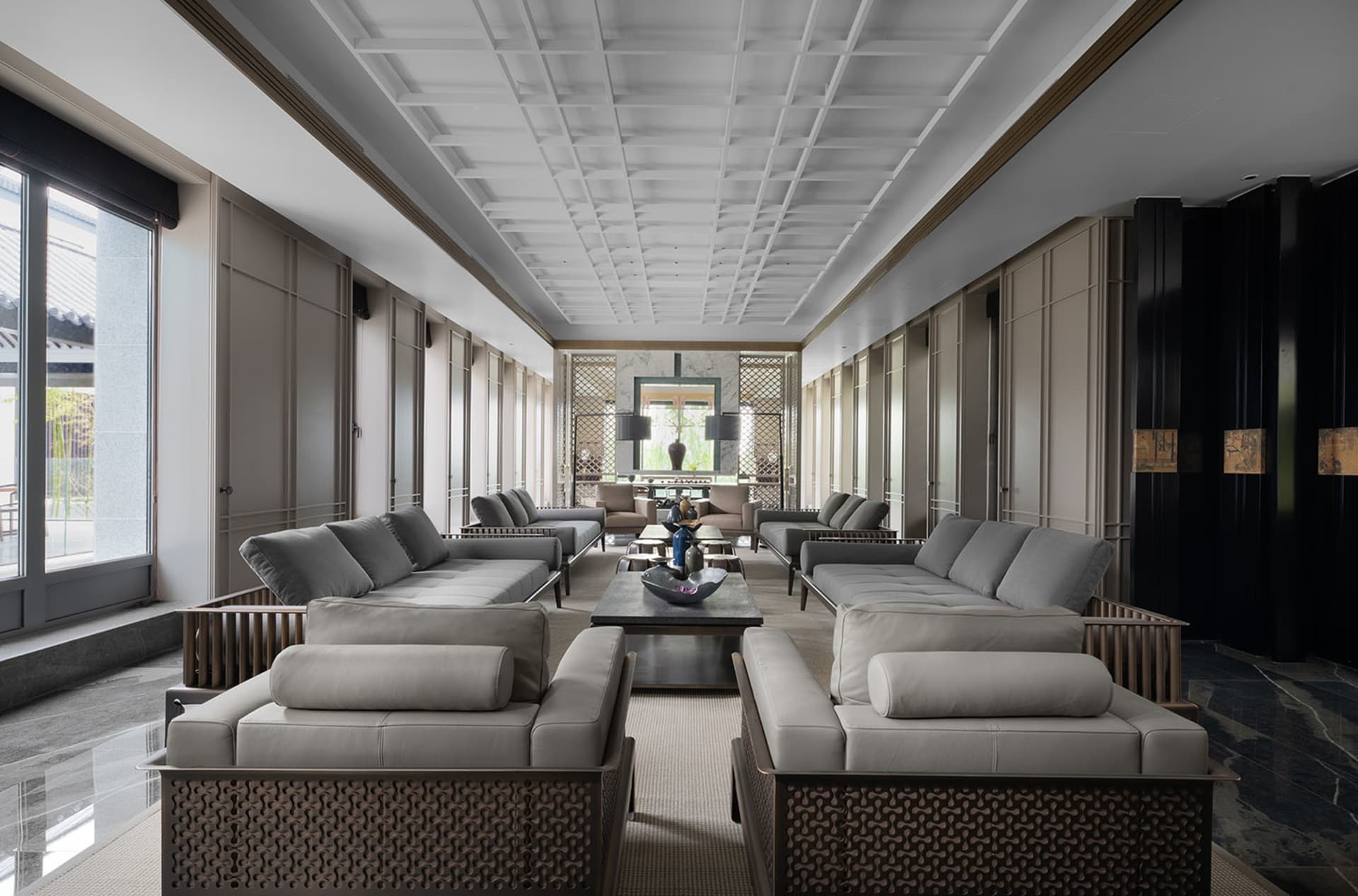 A spacious, modern residential interior featuring textured leather sofas, a center table with decorative items, and large win