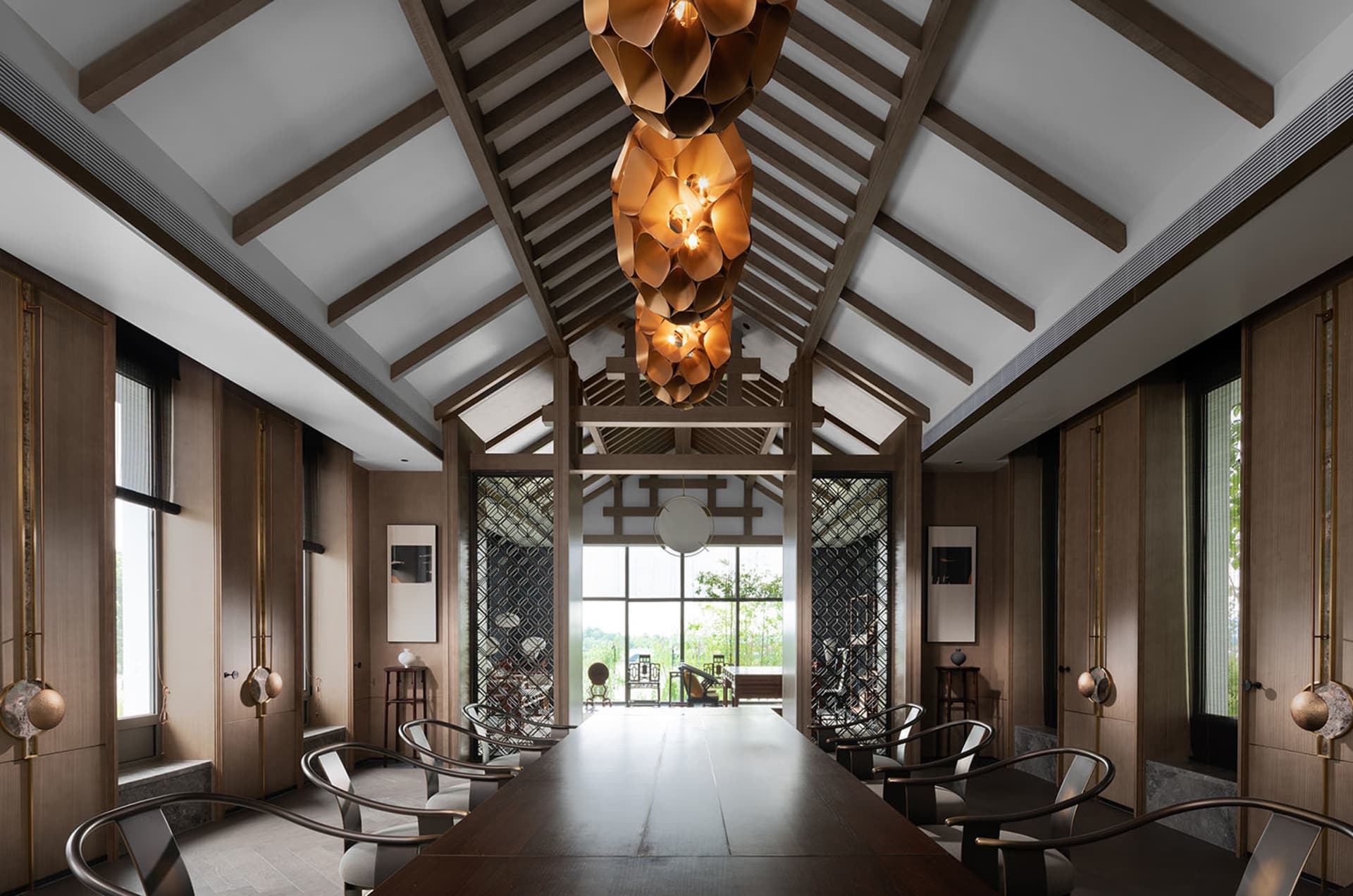 A spacious lounge with a high ceiling, wooden flooring, and large windows showcasing outdoor scenery.