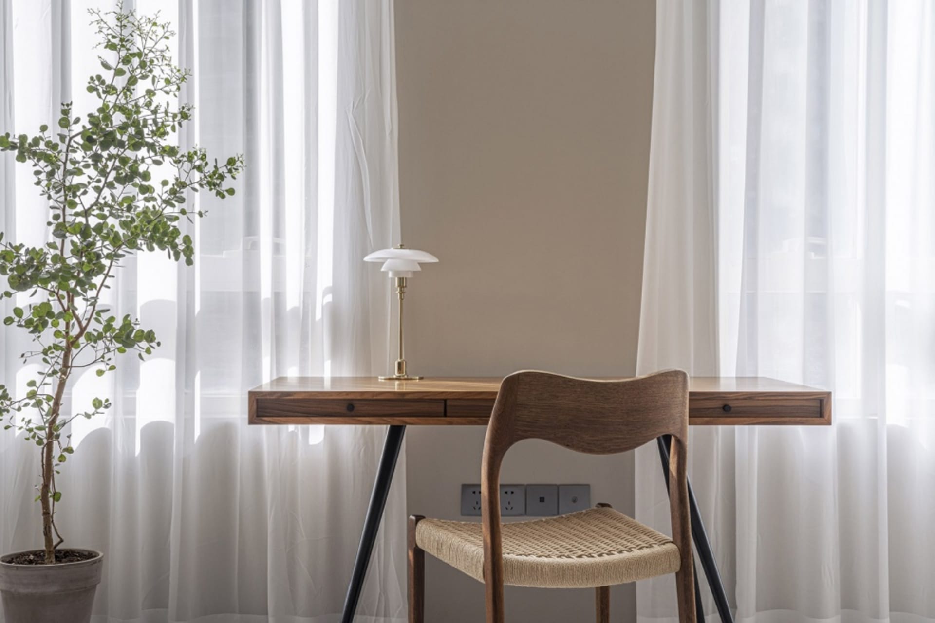 Modern minimalist home office with a wooden desk and white curtains.