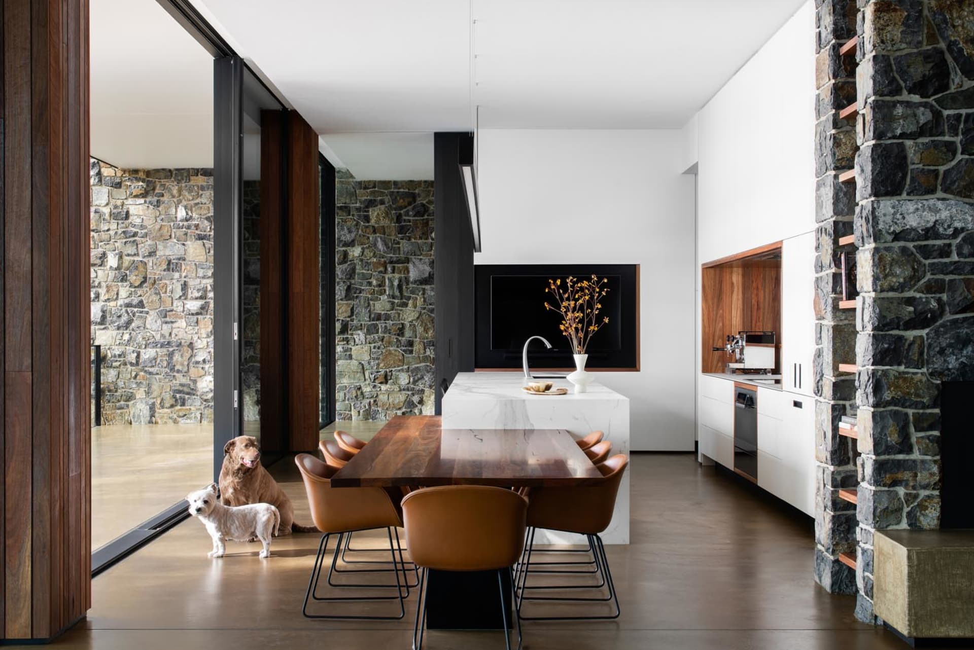 Modern dining room with marble table, timber chairs, and stone walls.
