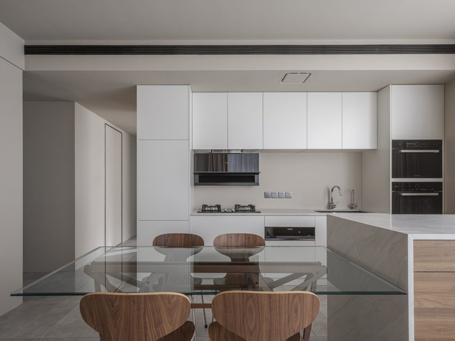 Modern kitchen with white cabinets, concrete countertops, wooden furniture, and a glass table top.