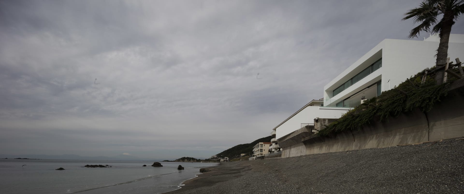 A modern residential building on a beach, with a white exterior and a concrete facade.