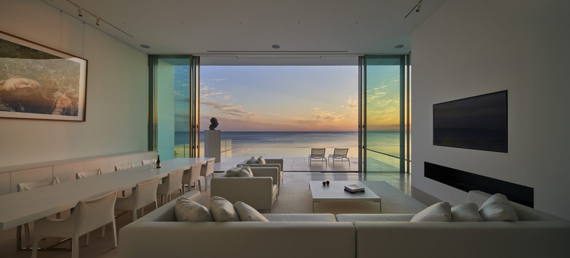 Modern living room featuring large glass doors overlooking the ocean at sunset.