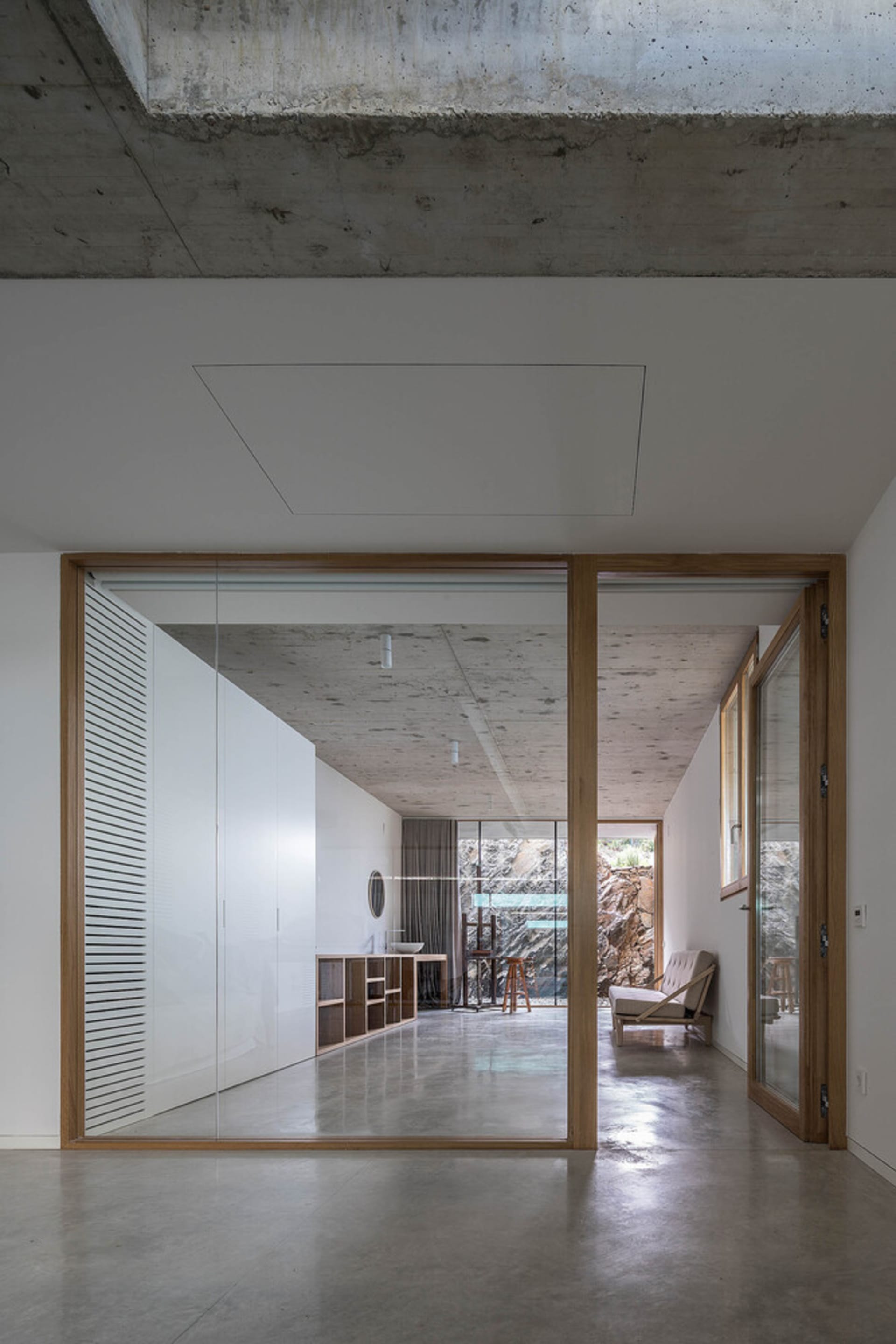 A minimalist bedroom with concrete walls and floor, featuring modern furniture and a large window.