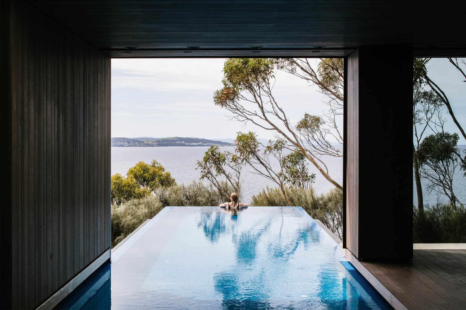 Person in a modern house with a glass infinity pool overlooking a teal-colored skyline.