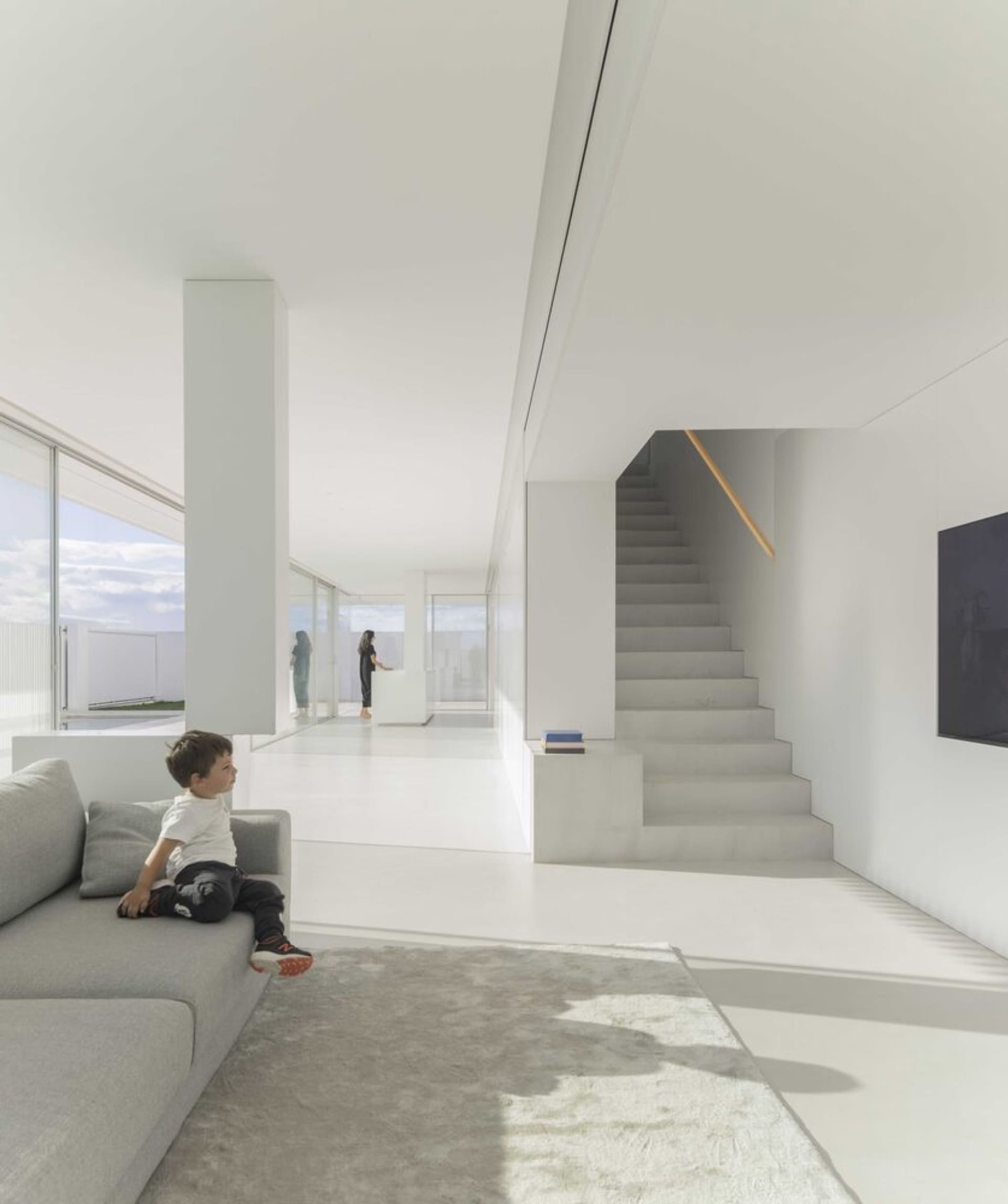 A minimalist living room with white walls, concrete floors, and a large window allowing natural light to fill the space.