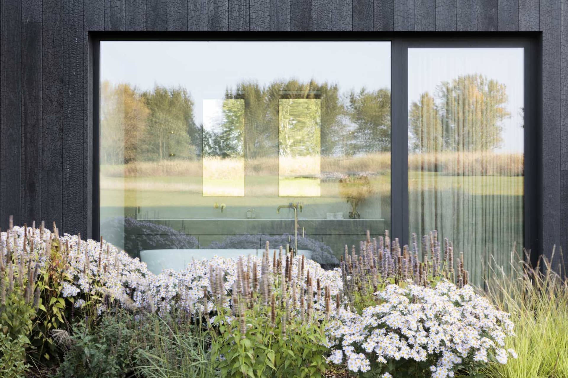 A modern bathroom with a glass bathtub overlooking a lush, flower-filled garden.