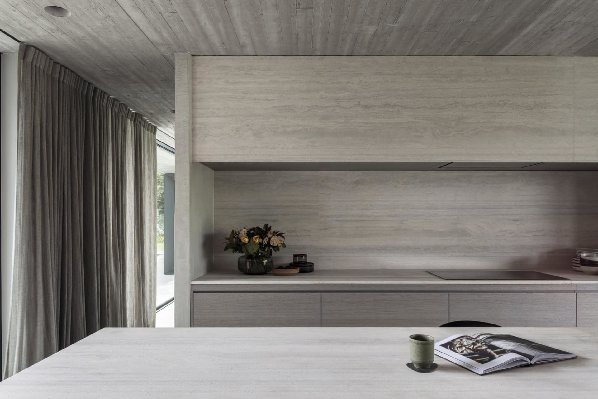 A modern, minimalist kitchen with concrete countertops and a large window.